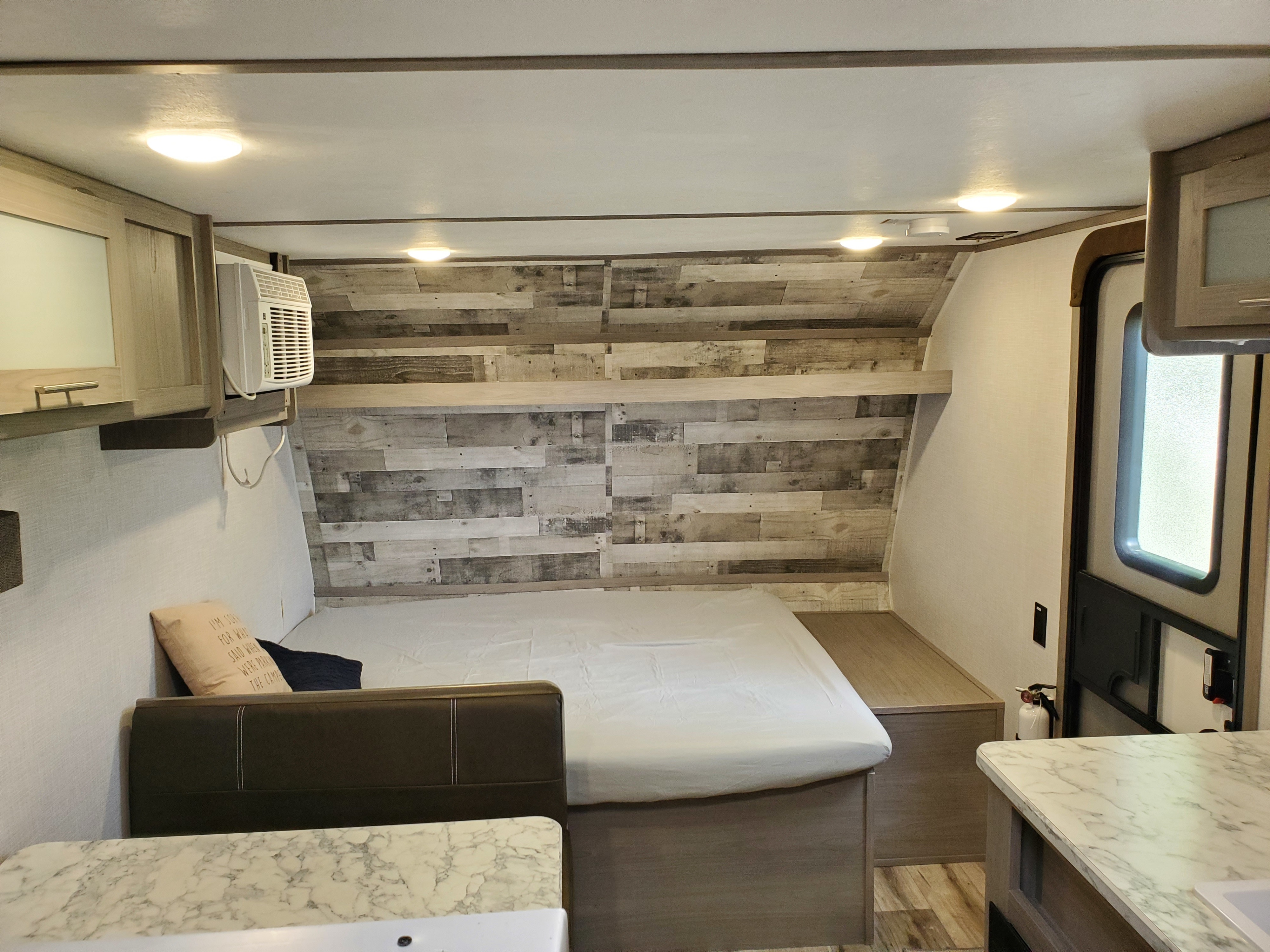 Inside a modern **rv rental**: a cozy bed with wood accent wall, overhead cabinets, AC, and marble countertop. Bright and functional interior.. Coleman LANTERN LT 17B 2022