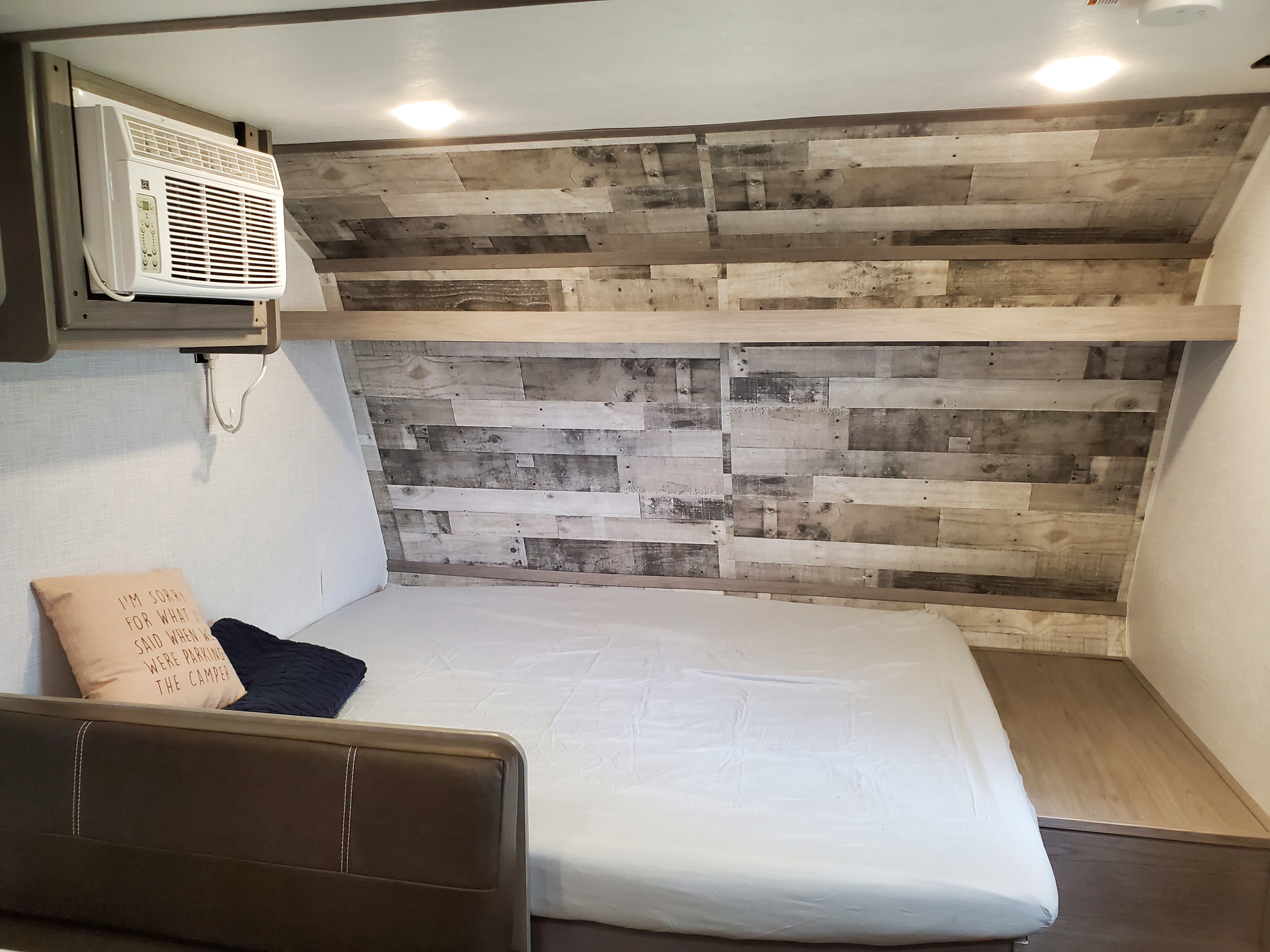 Cozy RV rental bedroom featuring a bed with white sheets, a decorative wood-paneled wall, and an overhead AC unit.. Coleman LANTERN LT 17B 2022