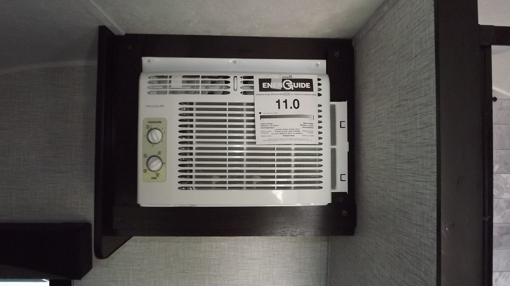 RV rental AC unit: A Frigidaire air conditioner with an 11.0 EnerGuide rating, mounted in a dark wooden frame in an RV.. Braxton Creek Bushwhacker 2022
