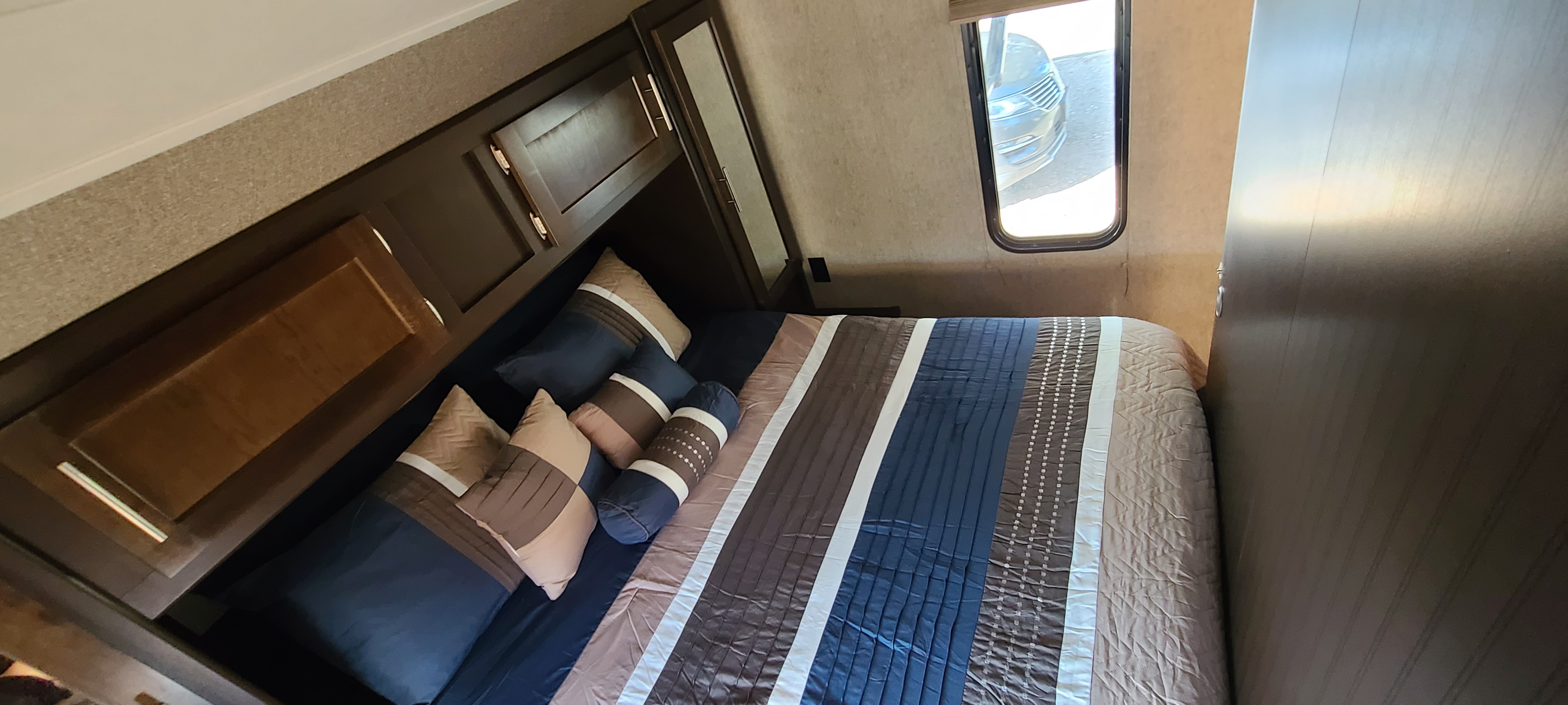 Comfortable RV rental bedroom featuring a neatly made bed with blue & brown bedding, decorative pillows, and overhead cabinets.. Forest River Cherokee Grey Wolf 2016