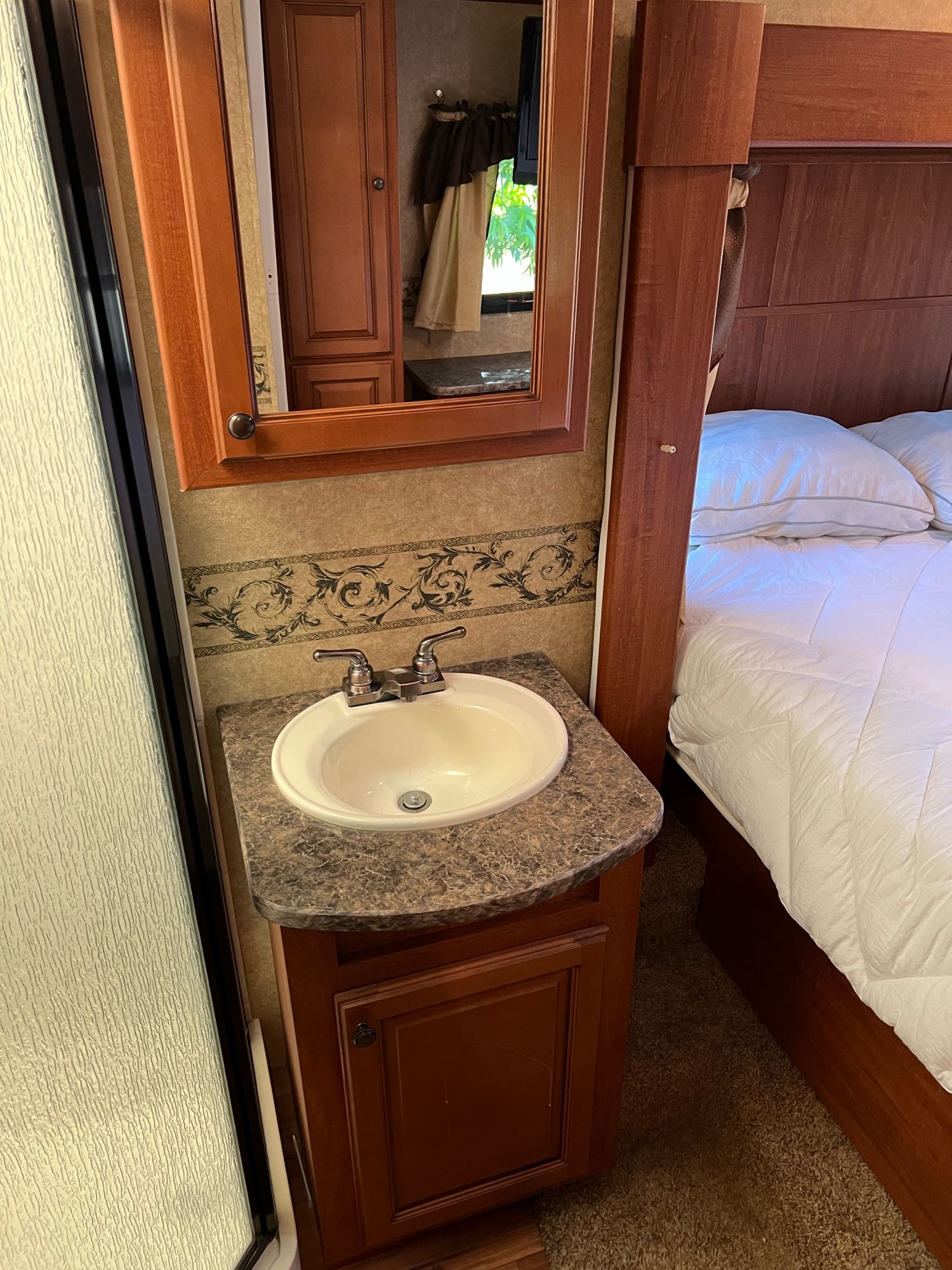 View of an RV rental's compact bathroom and bedroom area, featuring a sink, mirror, shower, and comfortable bed.. Heartland Greystone 2011