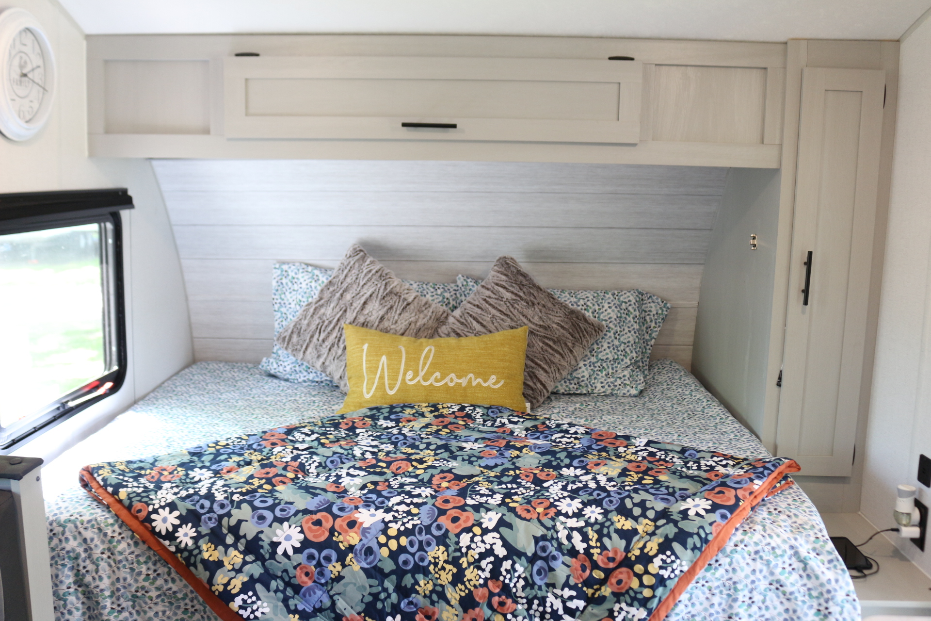 Inviting RV rental bedroom with a comfy bed, floral quilt, and "Welcome" pillow. Light wood cabinets complete the cozy space.. Forest River Wildwood FSX 2021