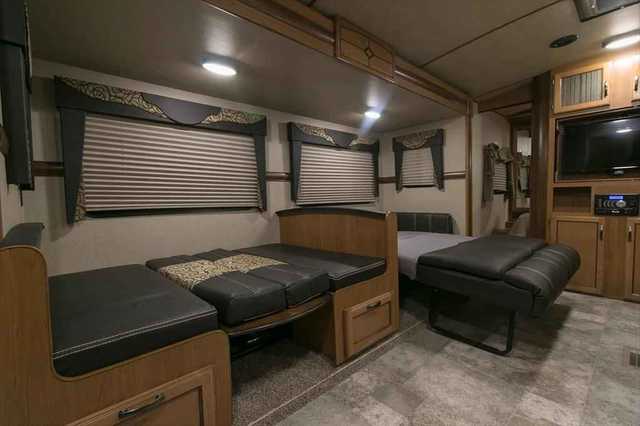 Inside this RV rental: A compact living area showing convertible beds/seating, windows with blinds, and entertainment center.. Crossroads RV Sunset Trail Super Lite 2018