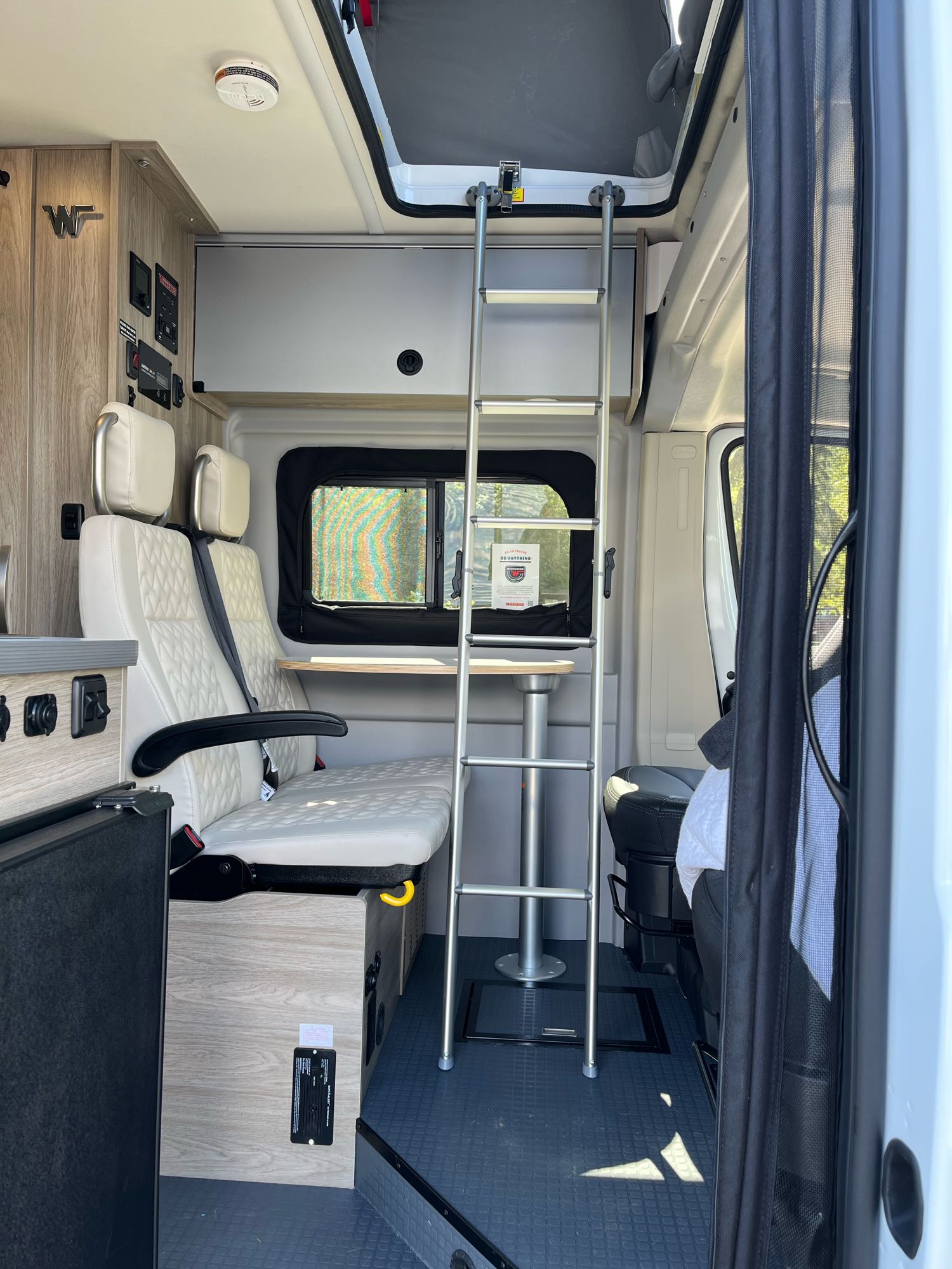 Spacious rv rental camper van interior. Features light seating, a movable table, and a ladder to a comfortable upper bed.. Ram Winnebago Solis 2023