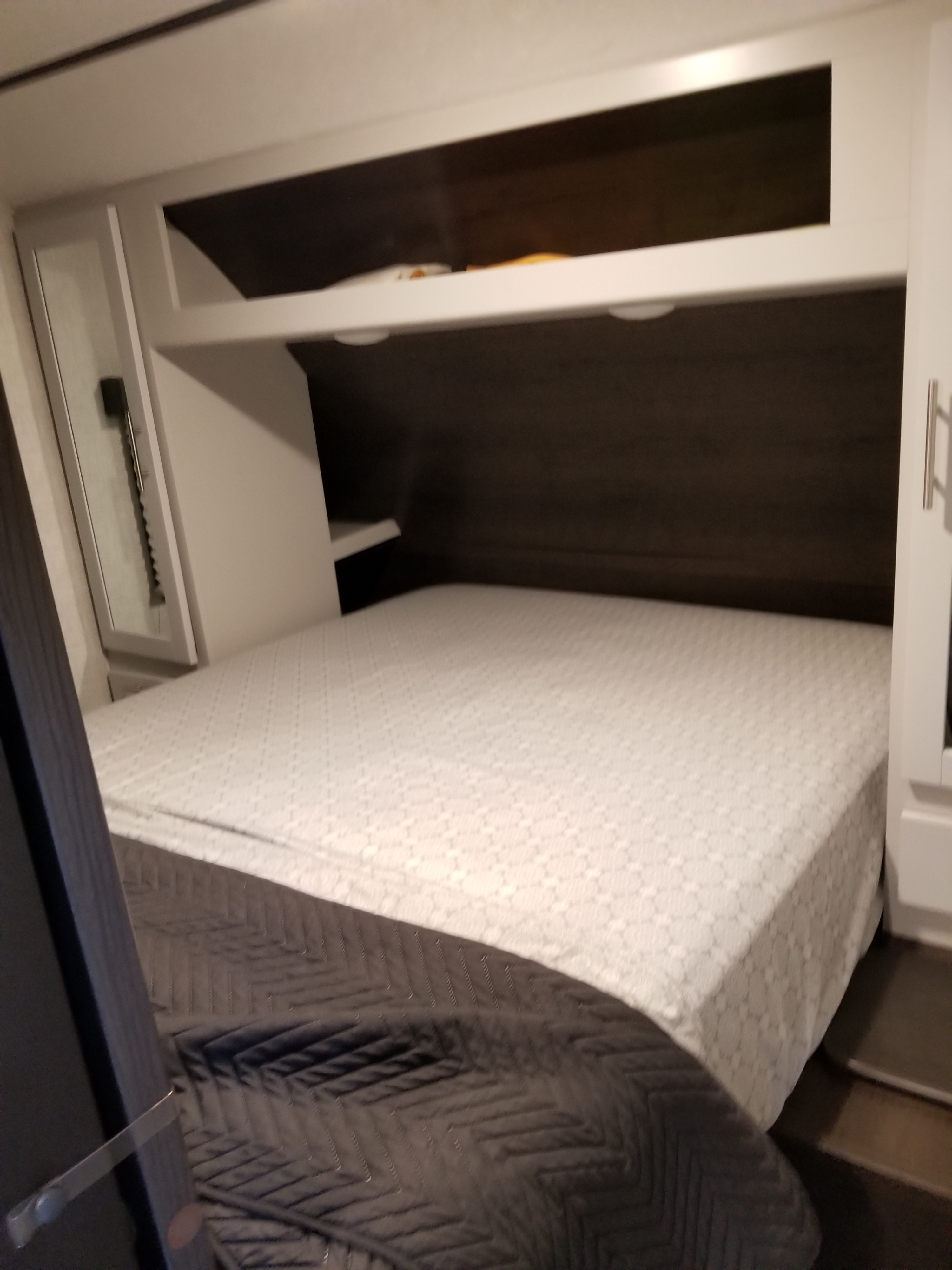 Cozy RV rental bedroom featuring a large bed with overhead storage and a mirrored cabinet, perfect for your next trip.. Keystone Bullet 2021