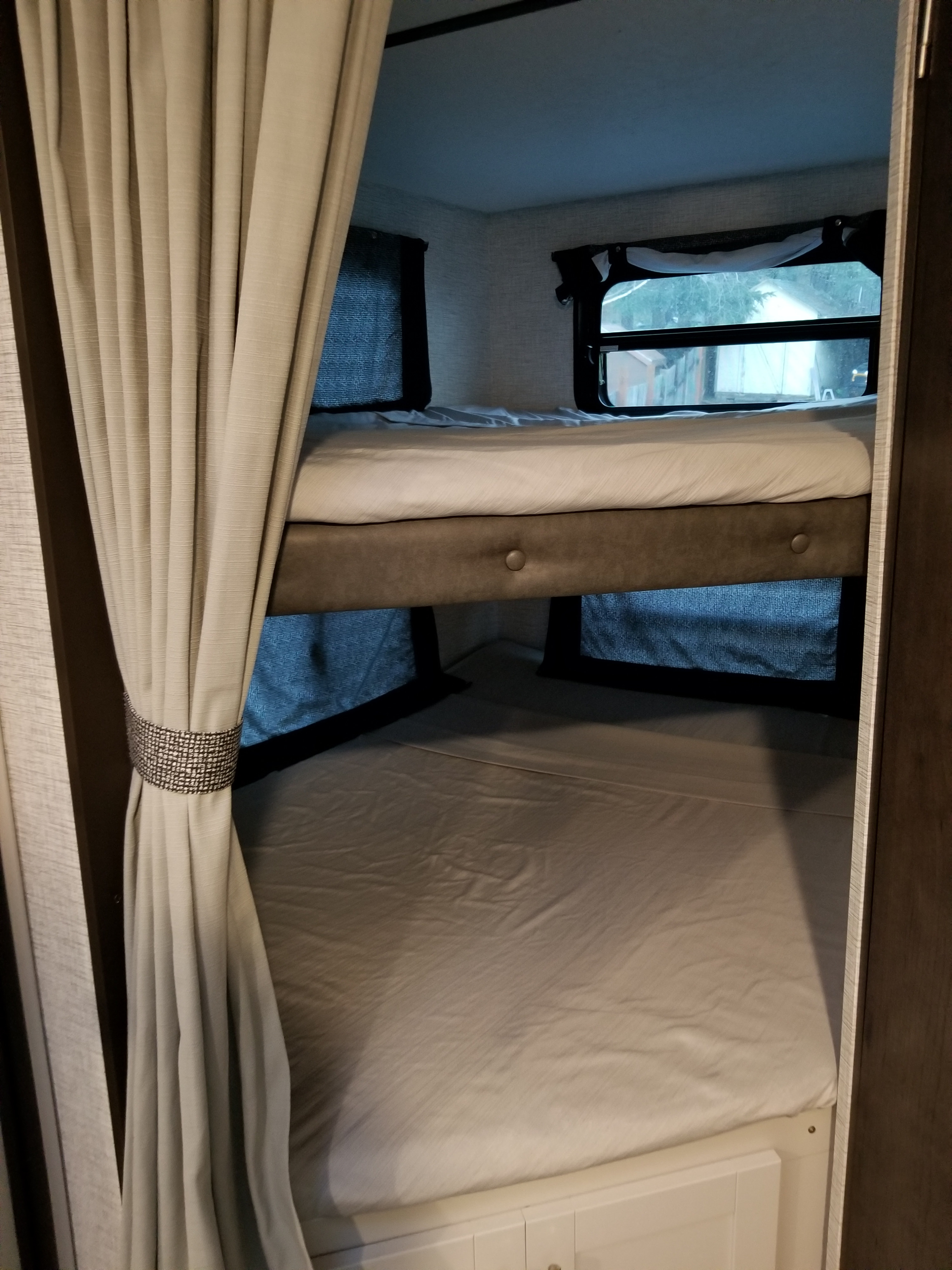 Inside an RV rental: cozy bunk beds with light sheets, windows, and a tied-back curtain for privacy.. Keystone Bullet 2021