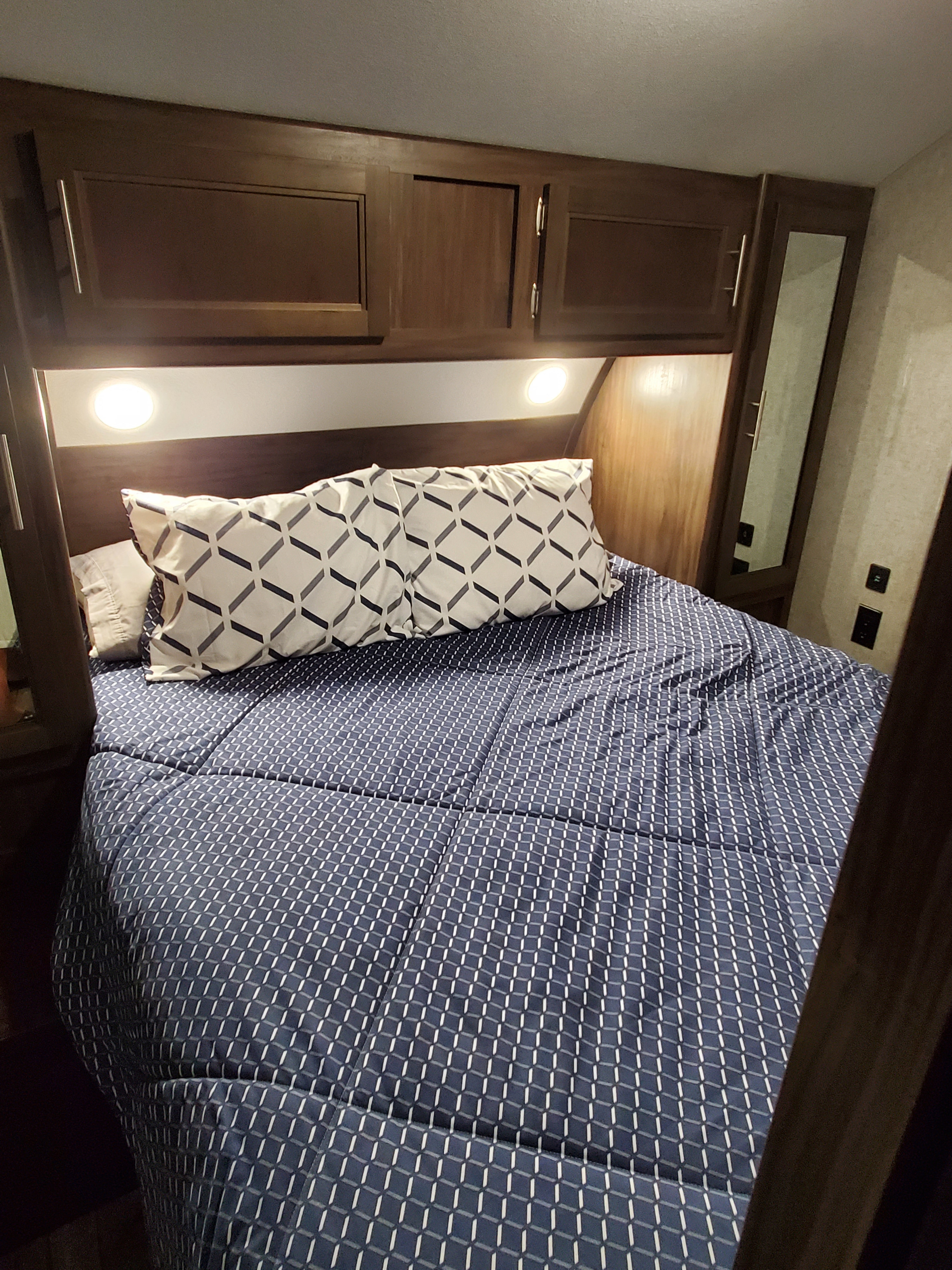 RV rental bedroom: a cozy bed with patterned comforter & pillows, overhead cabinets, and reading lights.. Forest River Cherokee Grey Wolf 2019