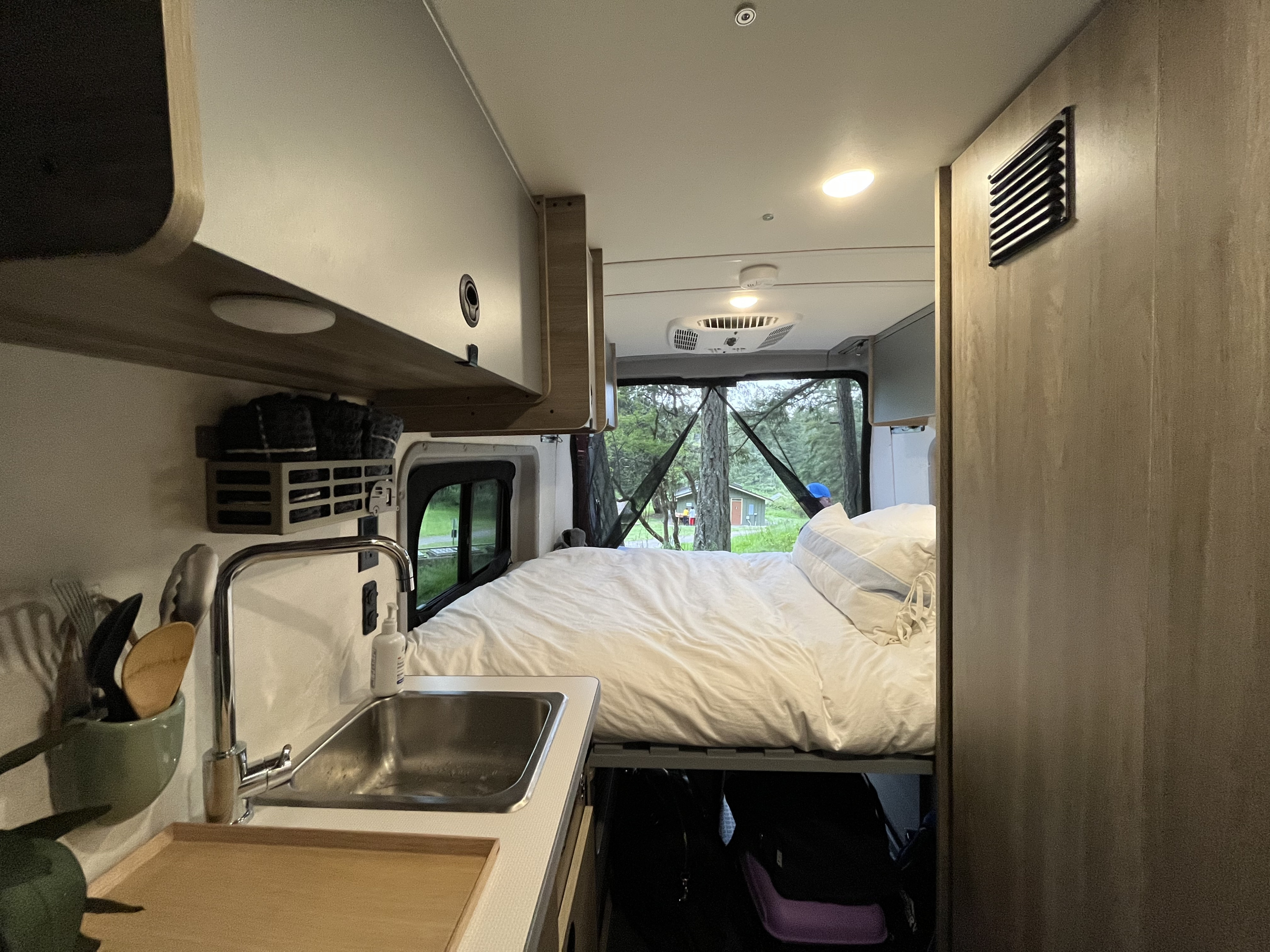 Cozy RV rental interior features a spacious bed, functional sink area, and scenic forest views from the rear window.. Winnebago Solis 59 PX 2023