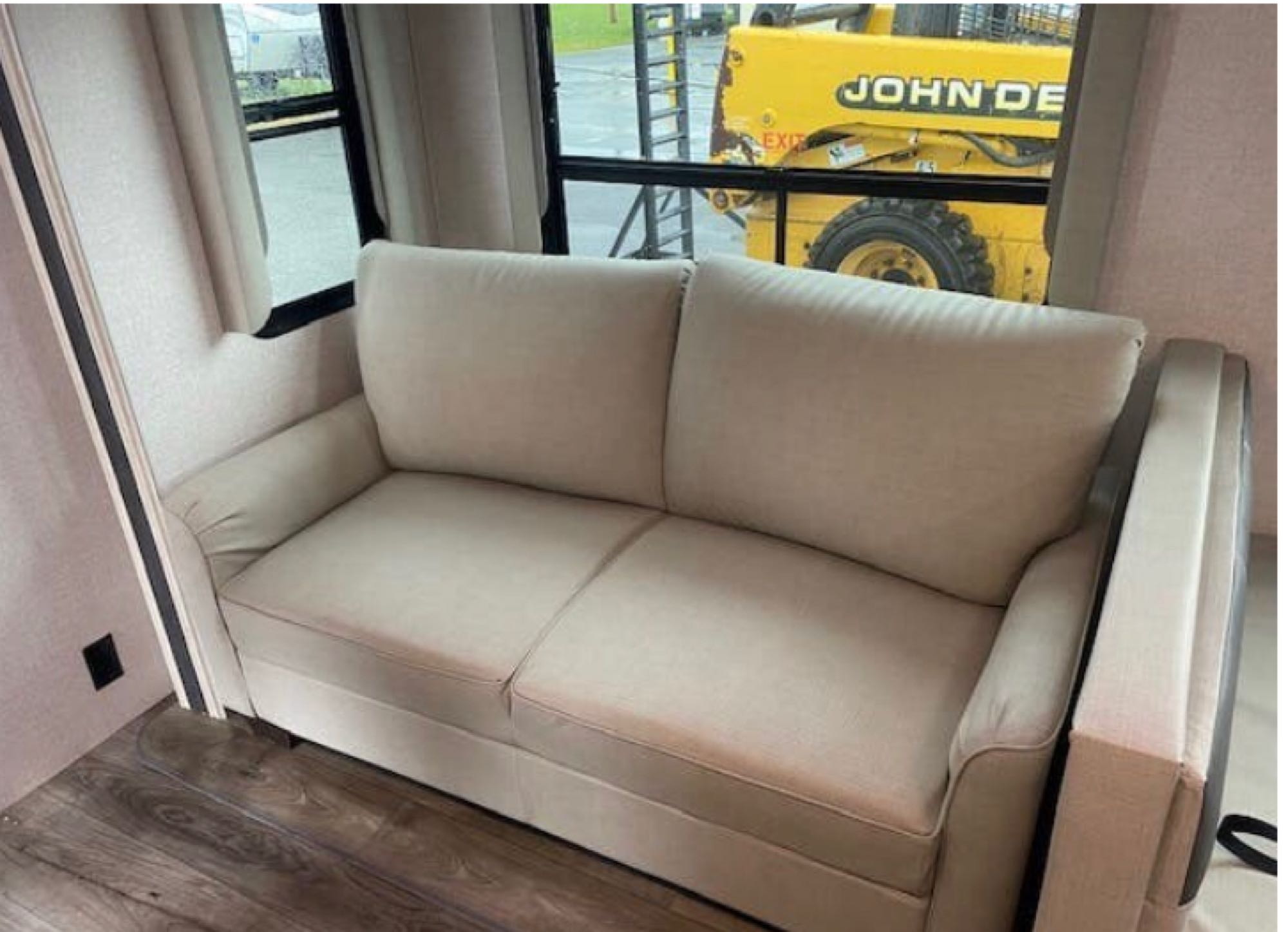 Cozy RV rental interior featuring a beige sofa, providing comfortable seating with a view of a John Deere outside.. Forest River East to West Alta 2022