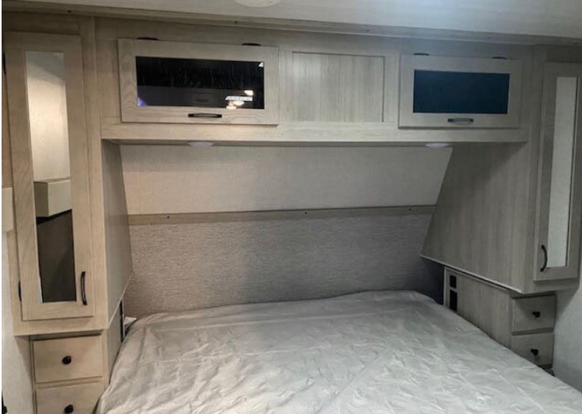 RV rental bedroom with light wood cabinetry, overhead storage, side closets, and a bed.. Forest River East to West Alta 2022
