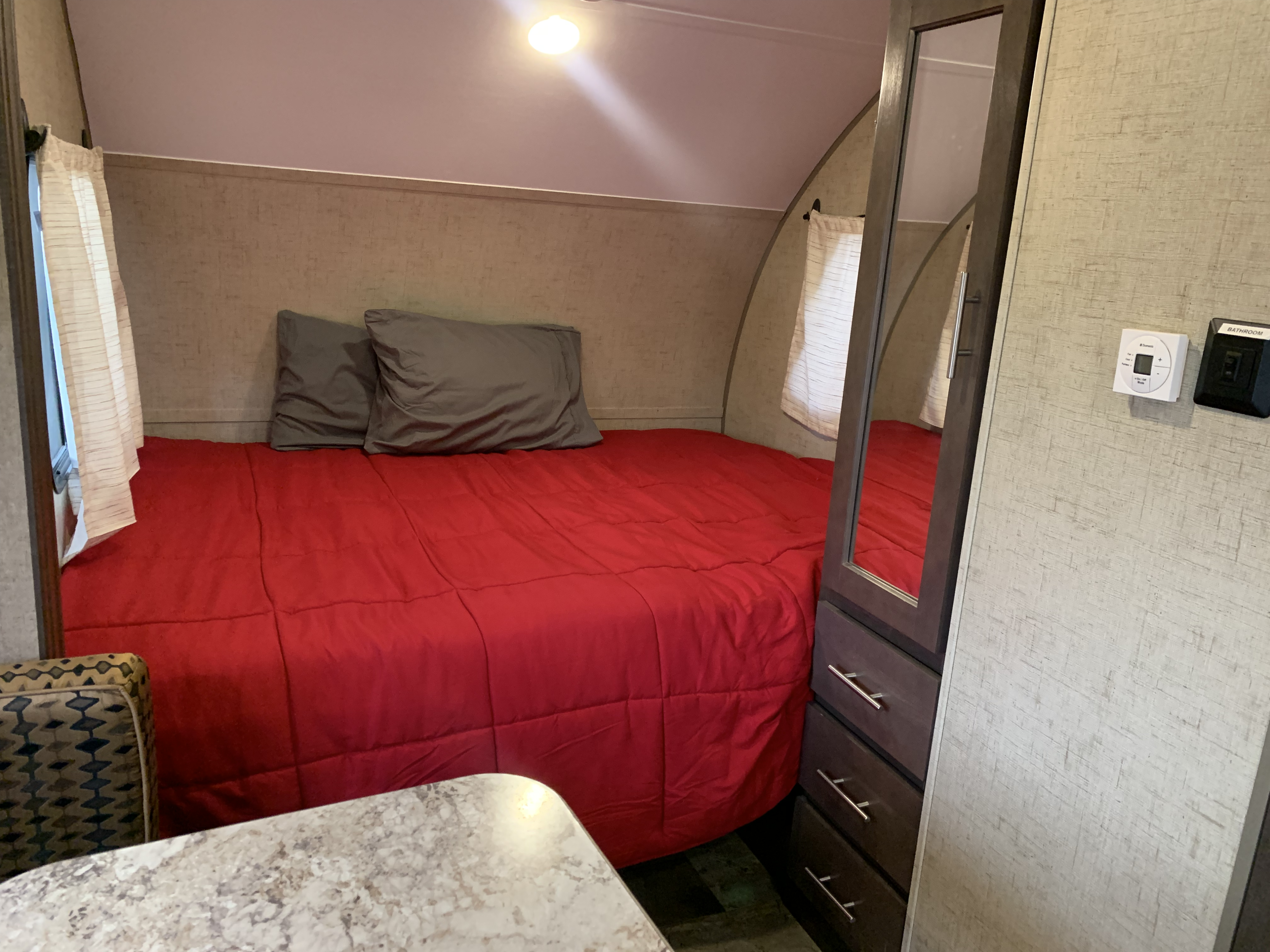 Cozy RV rental bedroom with a red bed, gray pillows, window curtains, and built-in storage. Ready for adventure!. Forest River R.POD TOWABLE 2016