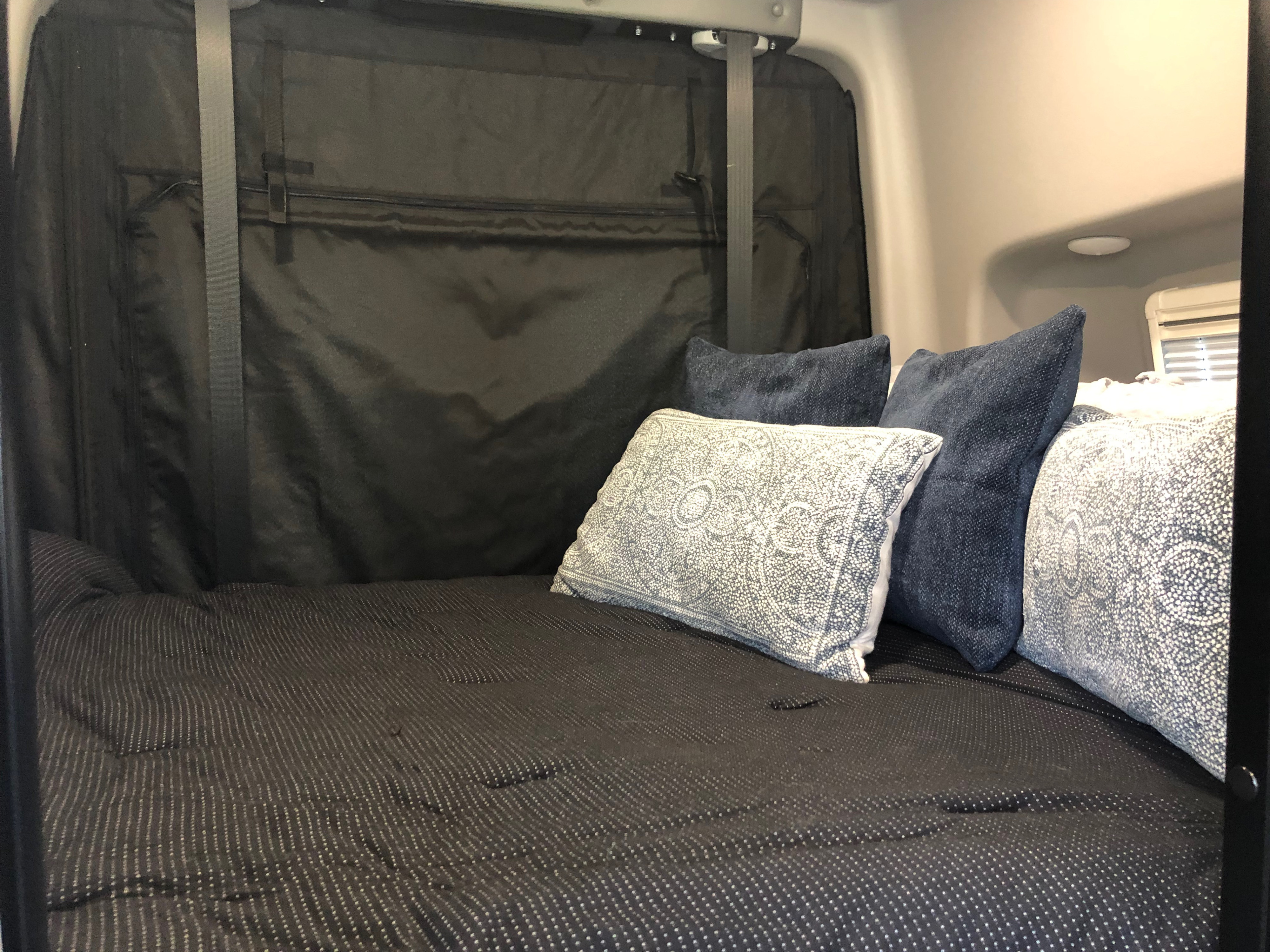 Comfortable RV rental bed with patterned comforter & throw pillows in a cozy interior, ideal for relaxation.. Winnebago Revel 2022