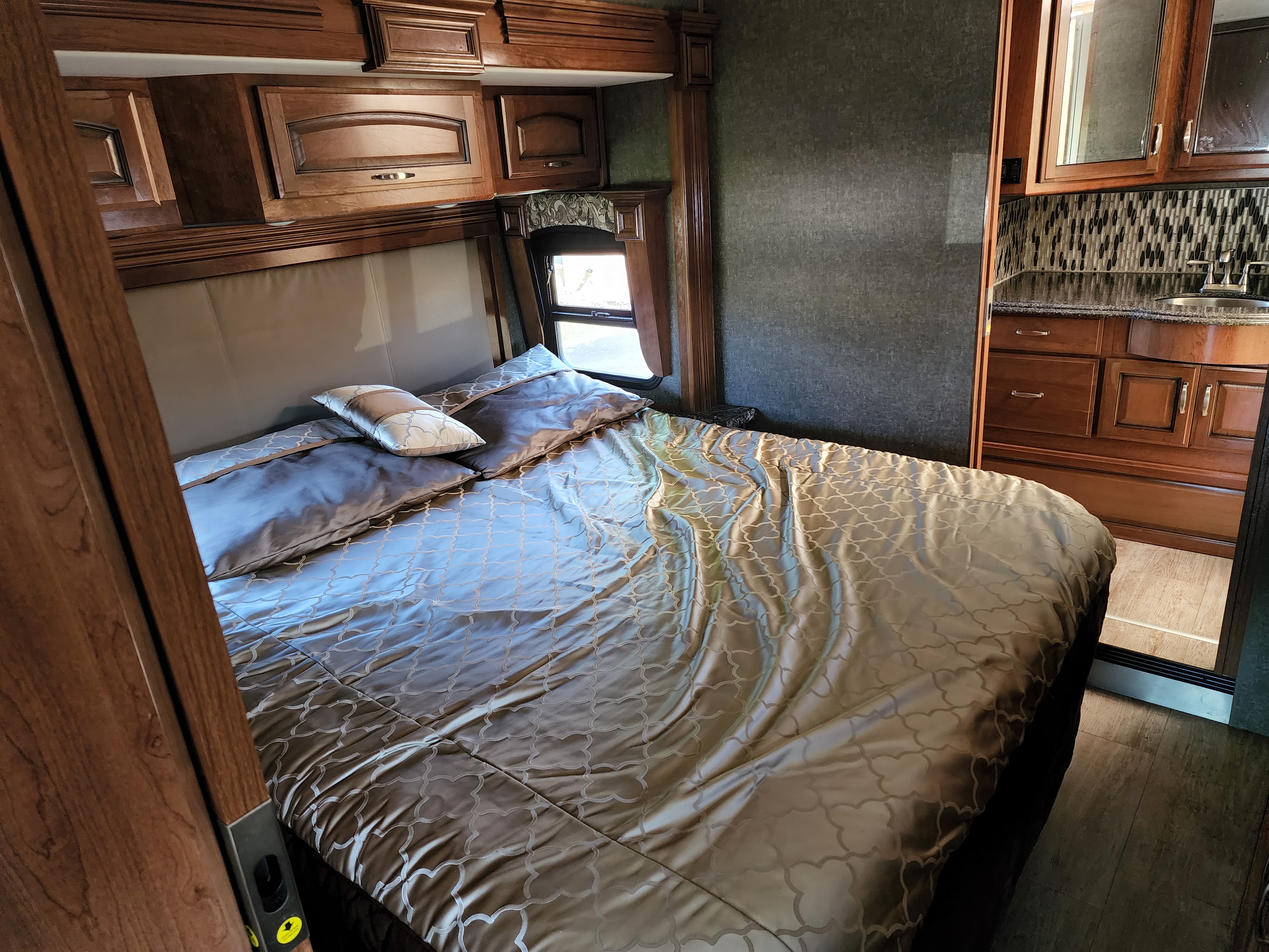 Comfortable RV rental bedroom featuring a large bed with patterned bedding, wood cabinetry, and a compact sink area.. Holiday Rambler Navigator XE 2018