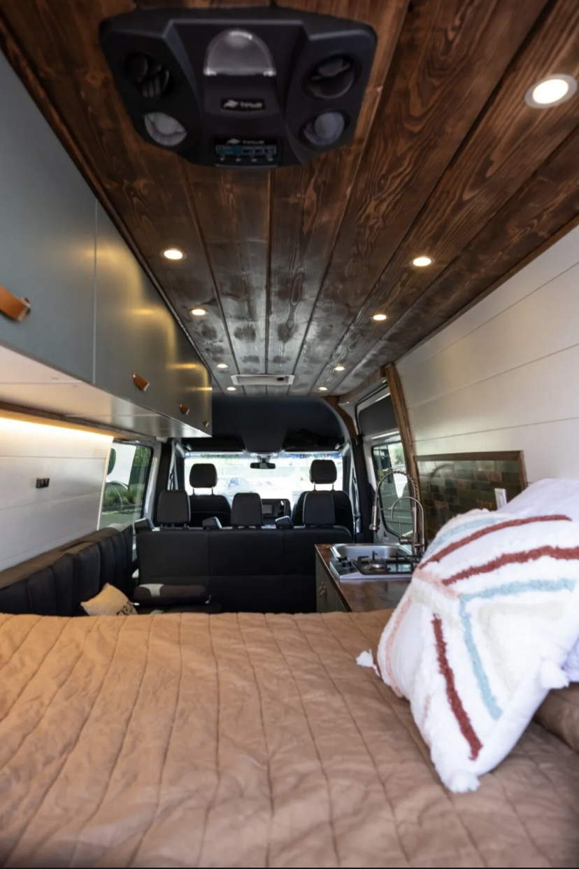Inside a spacious RV rental: cozy bed, compact kitchen, and elegant wood ceiling. Ideal for trips.. Mercedes Sprinter 2019