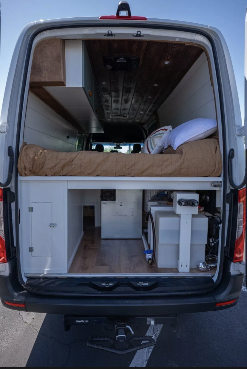 RV rental: Custom camper van interior with a cozy raised bed, clever storage, and wood accents.. Mercedes Sprinter 2019