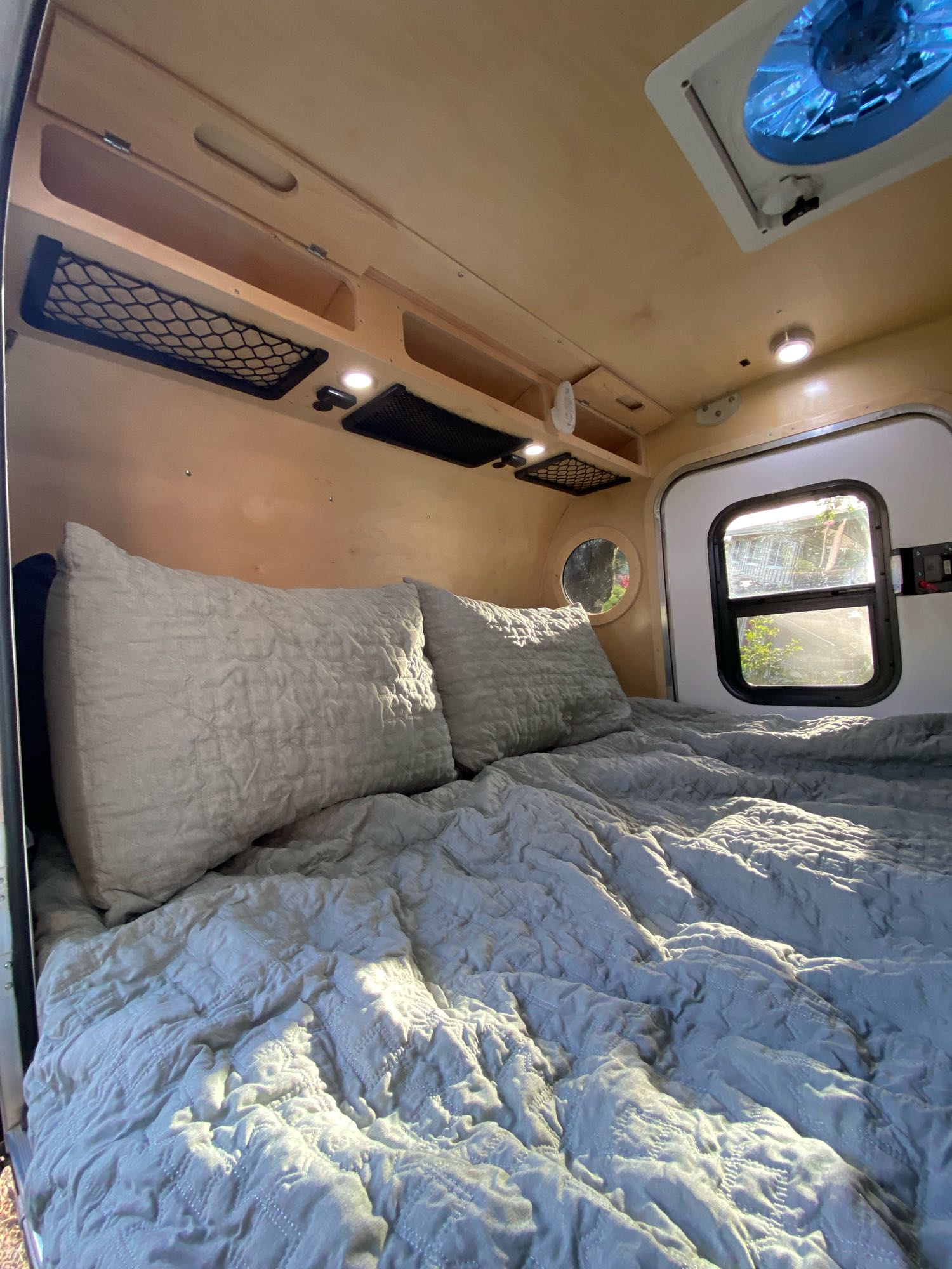 Cozy interior of an RV rental showing a comfortable bed, wooden walls, and natural light from a window.. Teardrops Northwest Trek 2022