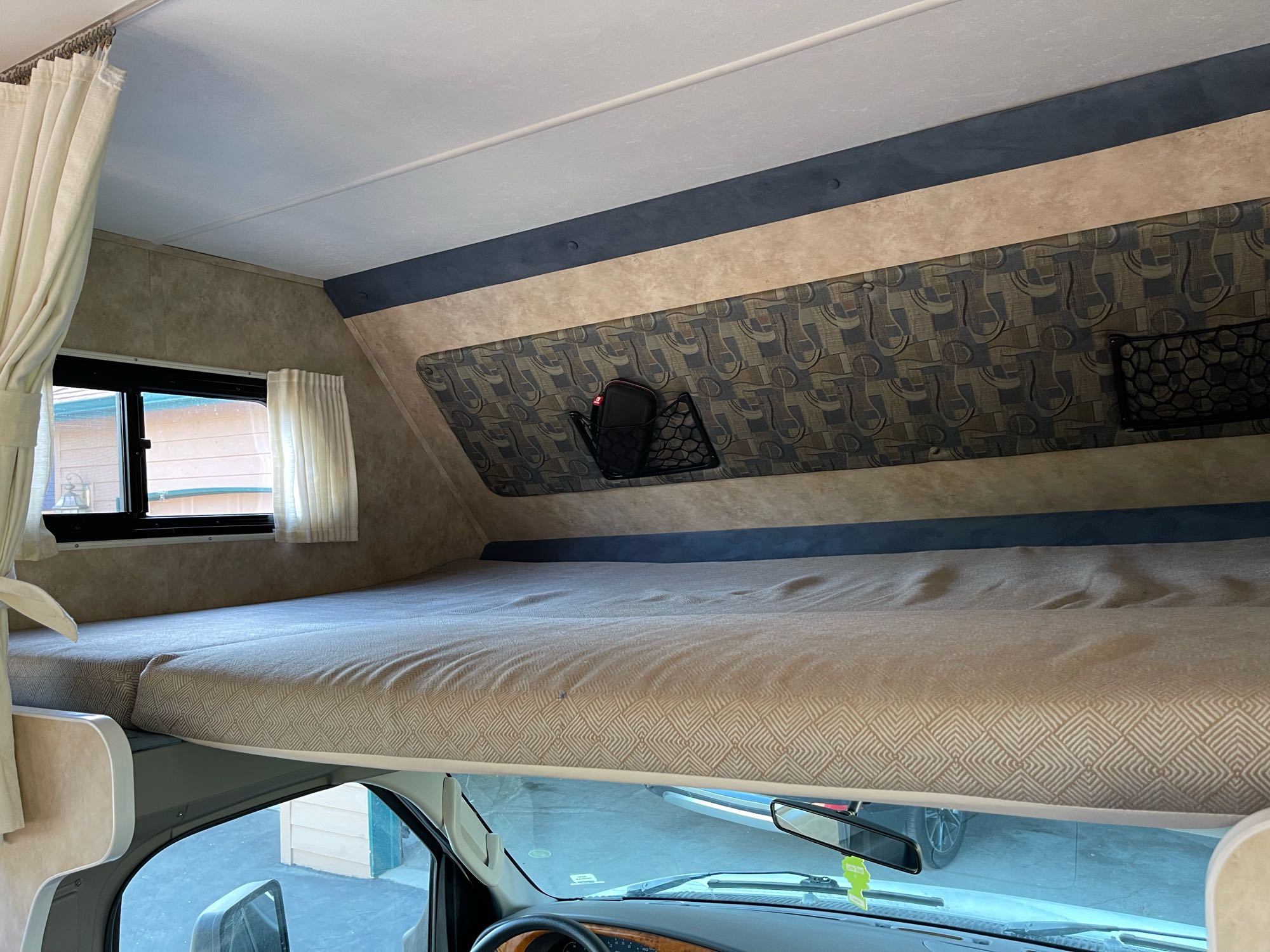 RV rental interior, showcasing a cab-over bunk bed with patterned mattress, storage net, and windows.. GULF W6211 2008