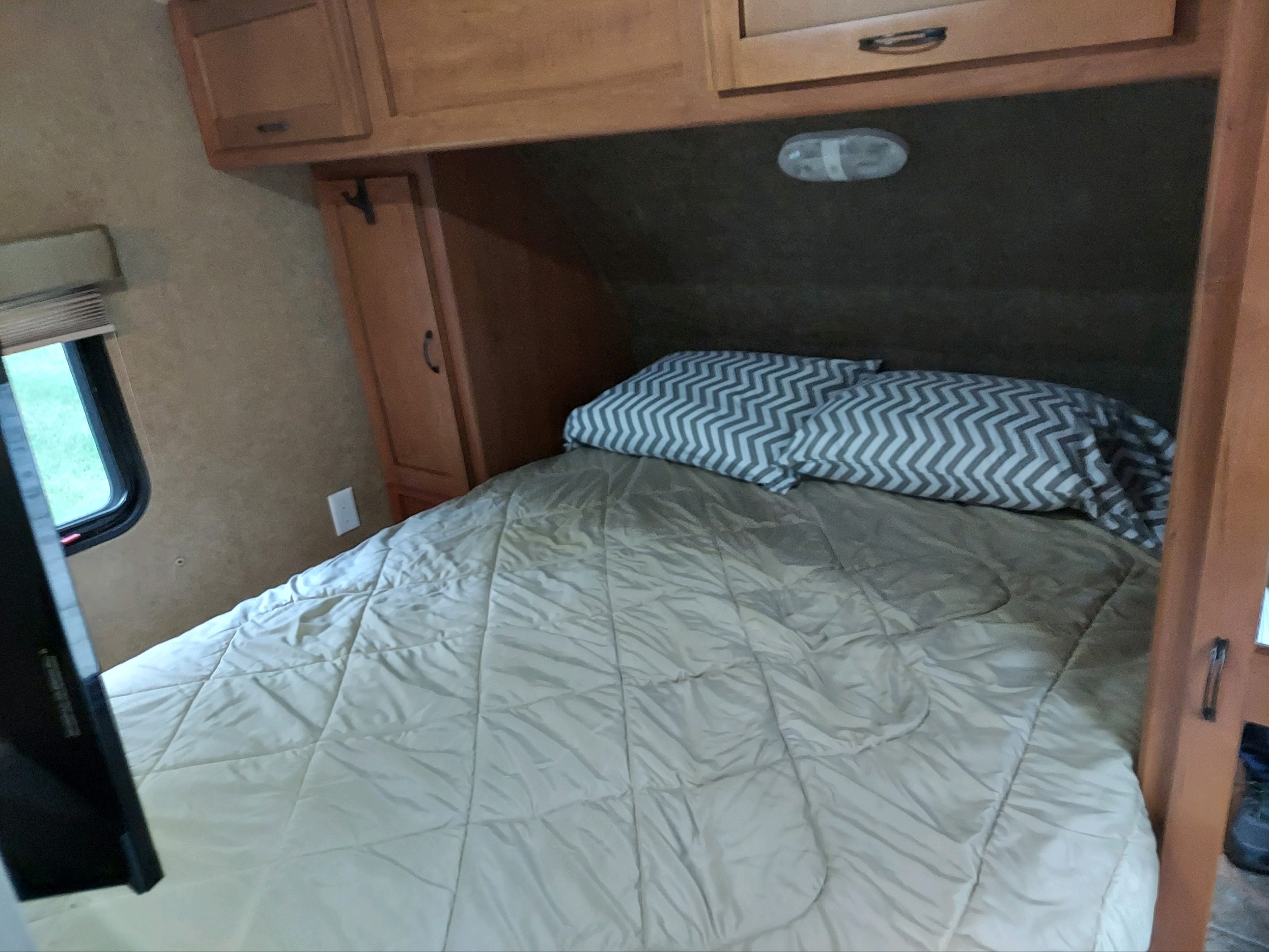 This cozy RV rental bedroom features a bed with patterned pillows, wooden cabinets, and a window.. Forest River Cherokee Grey Wolf 2014