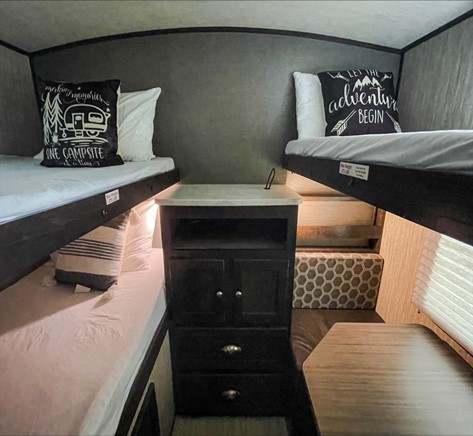 Interior of an RV rental: two bunk beds with decorative pillows, a central cabinet, and a dinette area.. Cruiser RV Shadow Cruiser 2018