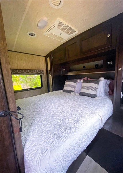 Comfortable RV rental bedroom featuring a neatly made bed, overhead storage, and a scenic window view.. Cruiser RV Shadow Cruiser 2018