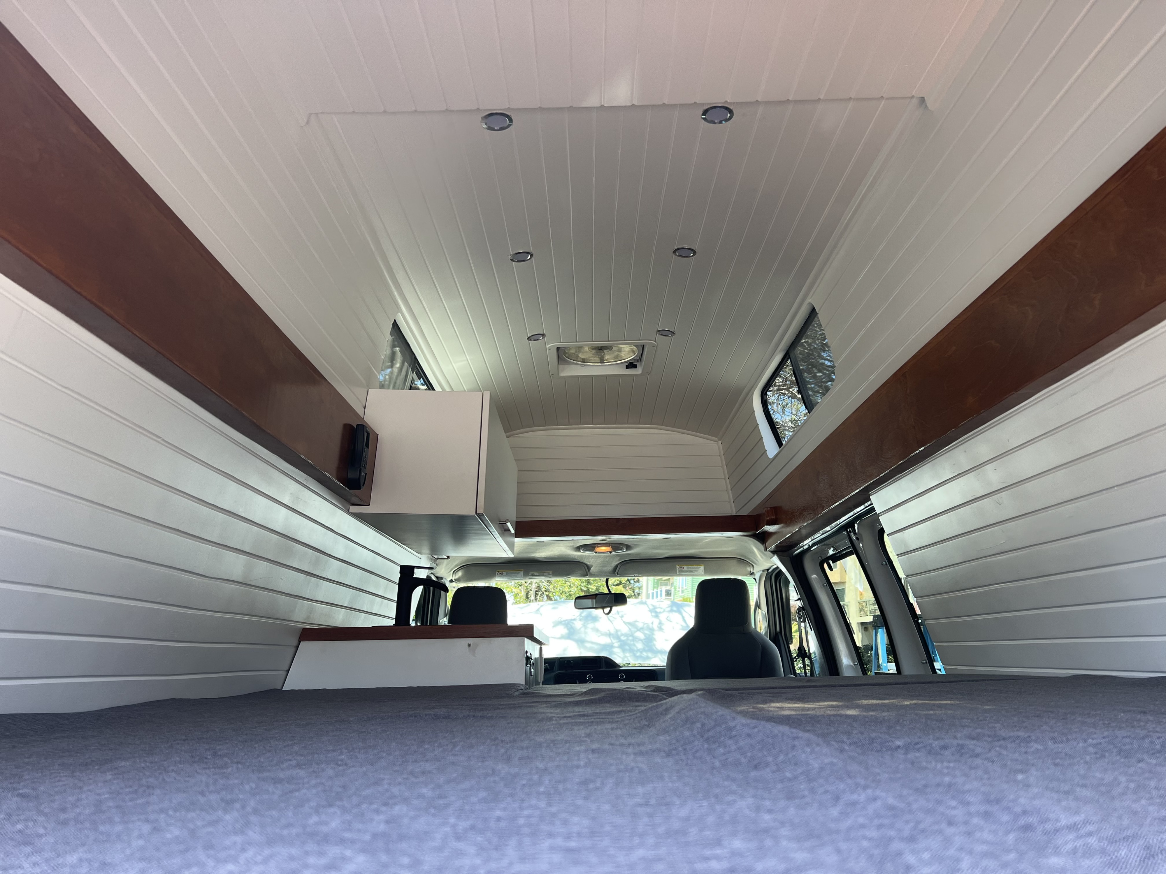 RV rental interior shows a converted campervan with white paneling, wood trim, bed, and ceiling fan, looking forward.. Ford Ford E350 2014