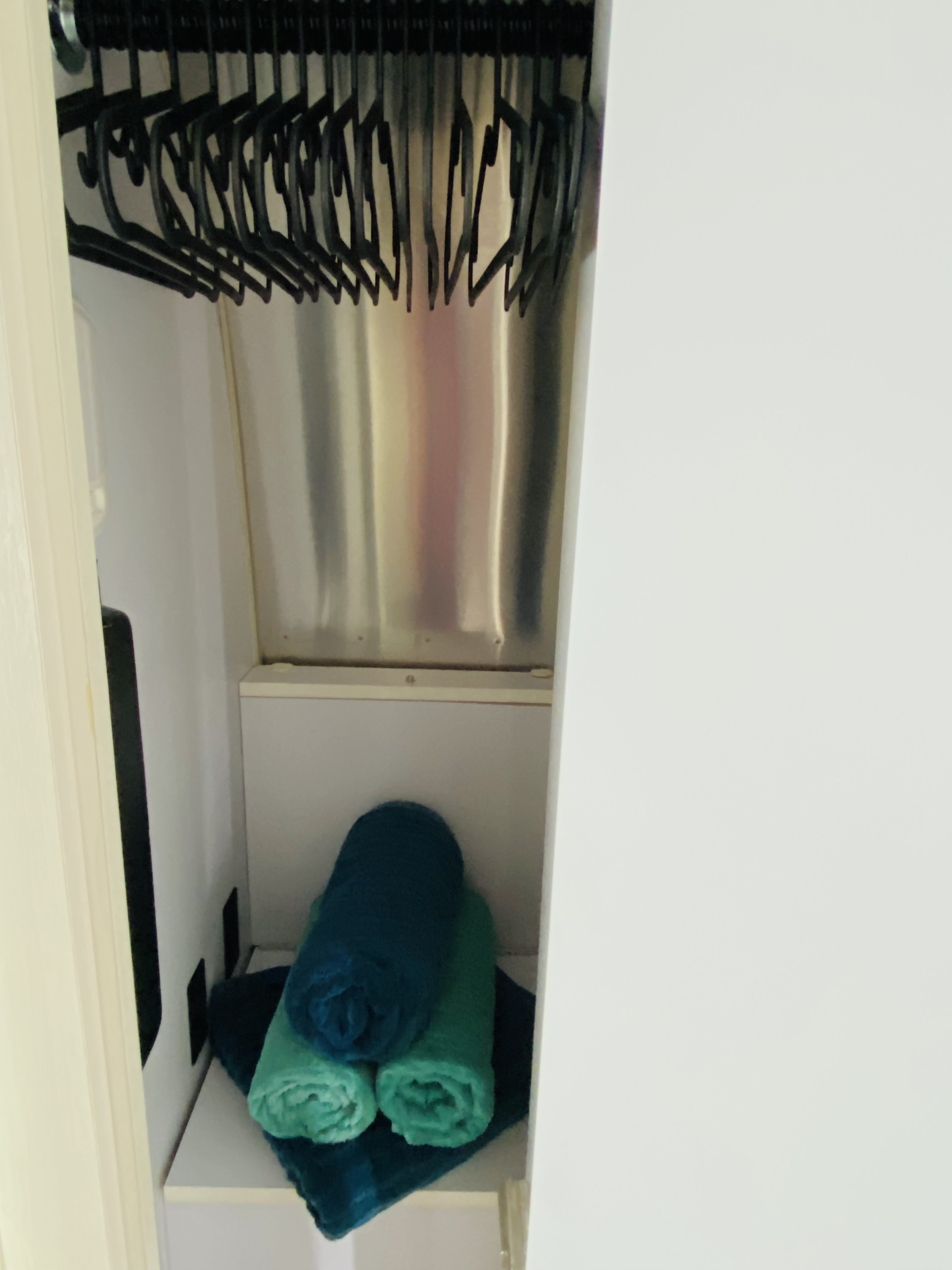 Compact RV rental closet: black hangers on a rod, with neatly rolled blue and green towels on a shelf.. Airstream Bambi 2020