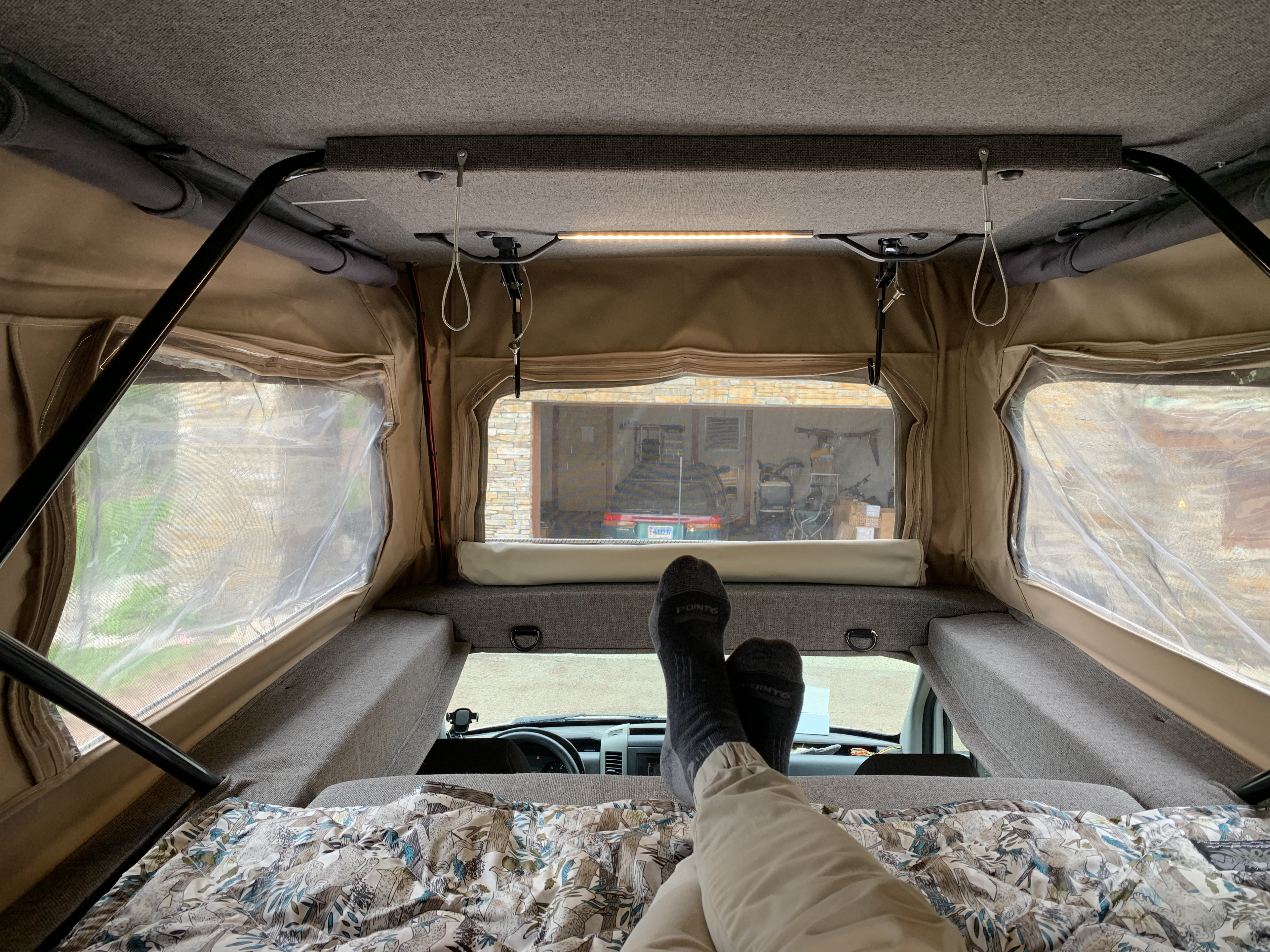 Relaxing inside a pop-top RV rental. View from a cozy bed reveals the camper's interior and outdoor scenery.. Sportsmobile Regular Body 2011