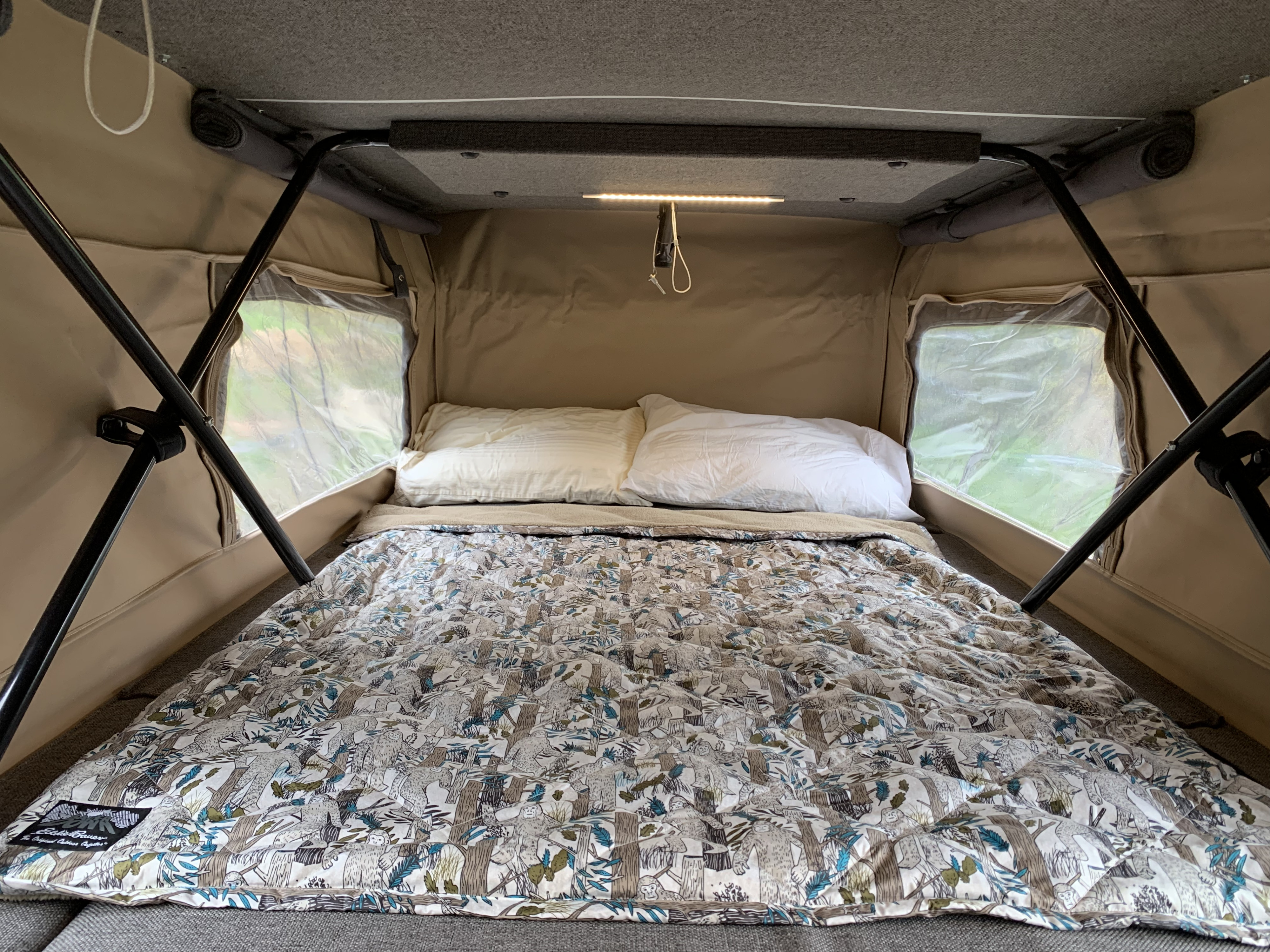 Cozy rv rental interior featuring a made bed with a unique patterned comforter, pillows, and bright windows.. Sportsmobile Regular Body 2011