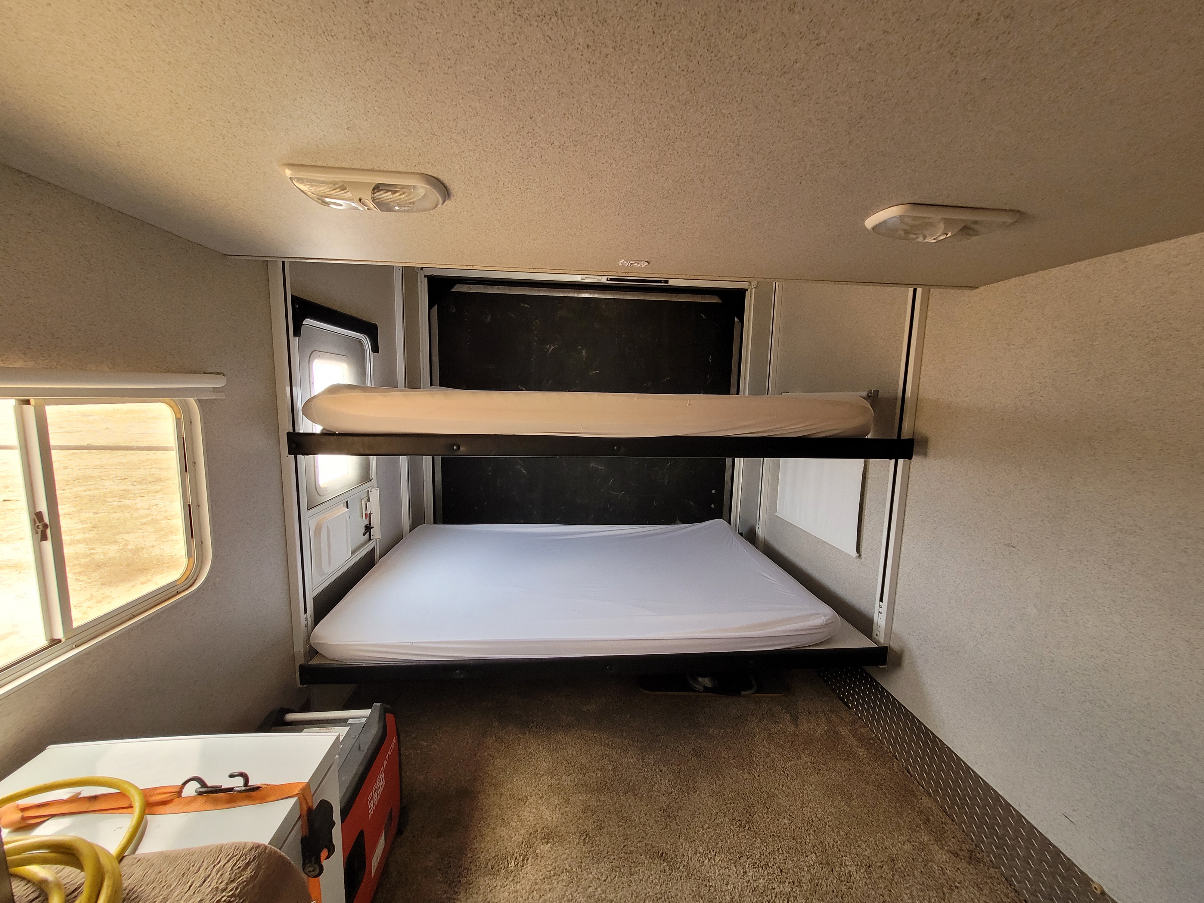 Interior of an RV rental: two stacked bunk beds with white mattresses, a window, and carpeted floor.. Heartland Cyclone 2009