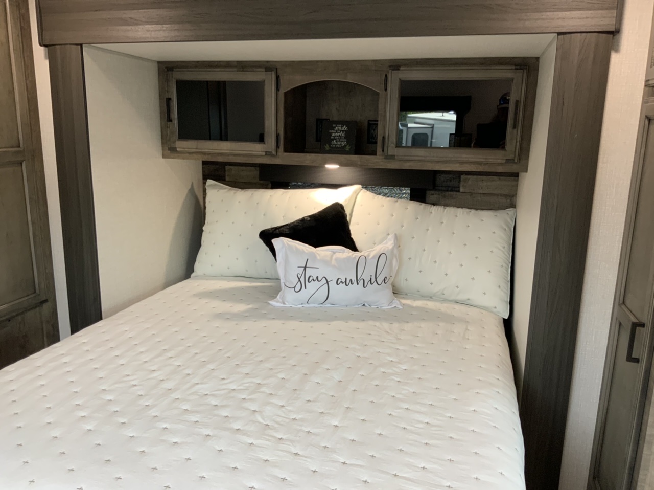 Cozy RV rental bedroom featuring a white bed with pillows, a "stay awhile" accent pillow, and overhead wood cabinetry.. Venture Rv Sporttrek 2027
