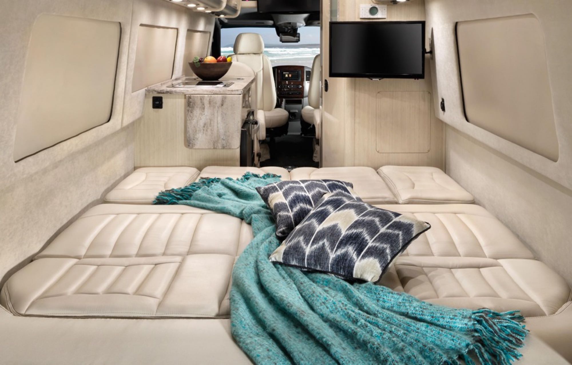 Enjoy this spacious RV rental camper van with a cozy bed, plush blanket, and a scenic beach view through the front.. Airstream Interstate 2015