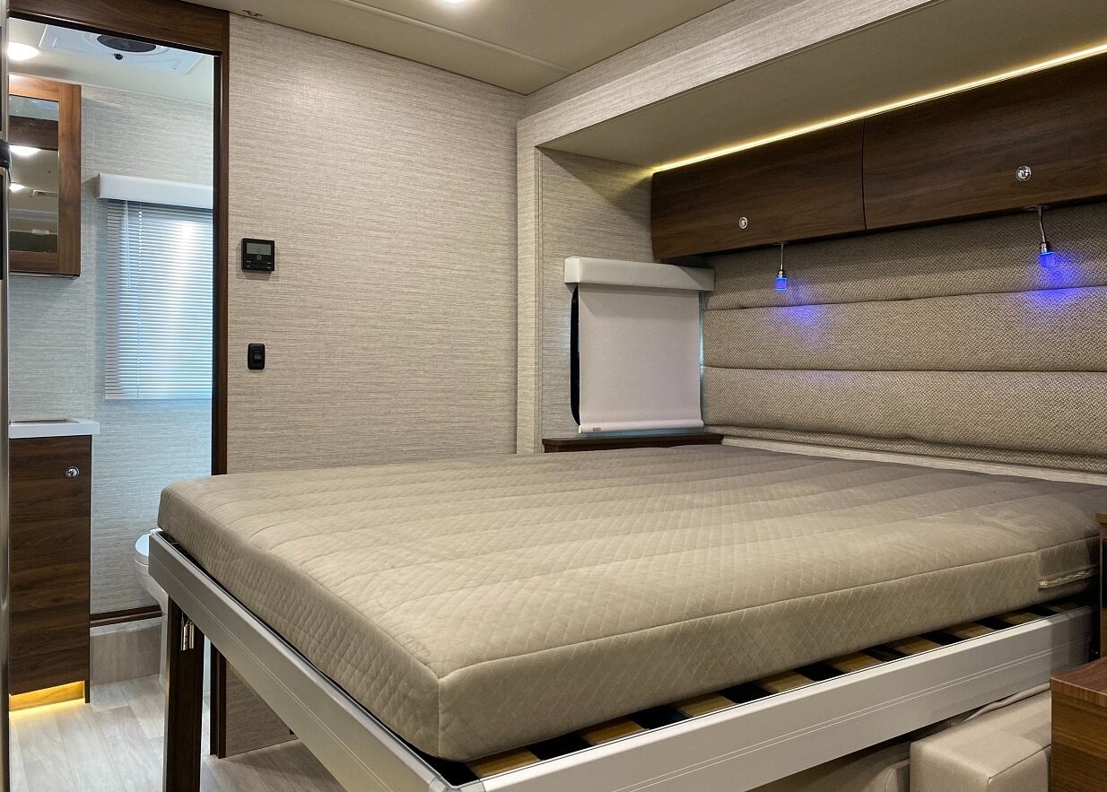 Modern RV rental bedroom with a comfortable bed, padded headboard, blue reading lights, and overhead storage.. Winnebago Navion 2022