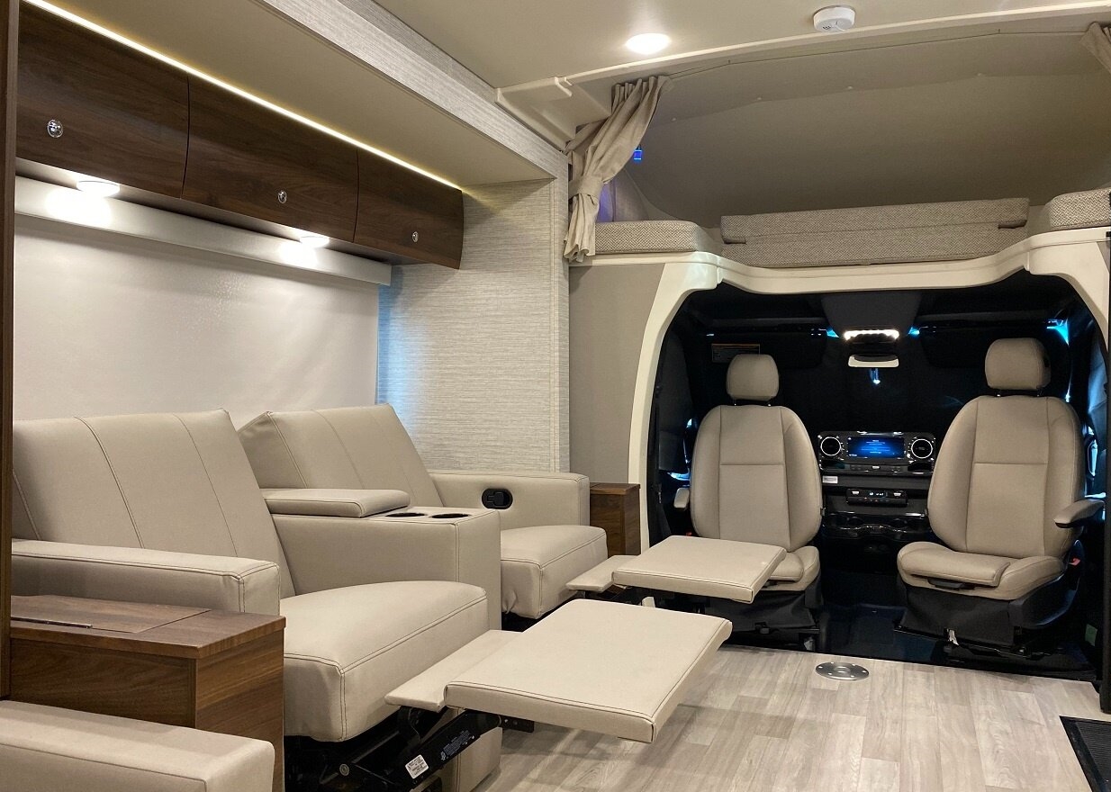Inside an RV rental: a spacious interior with light reclining seats, an overhead bunk, and the front cockpit.. Winnebago Navion 2022