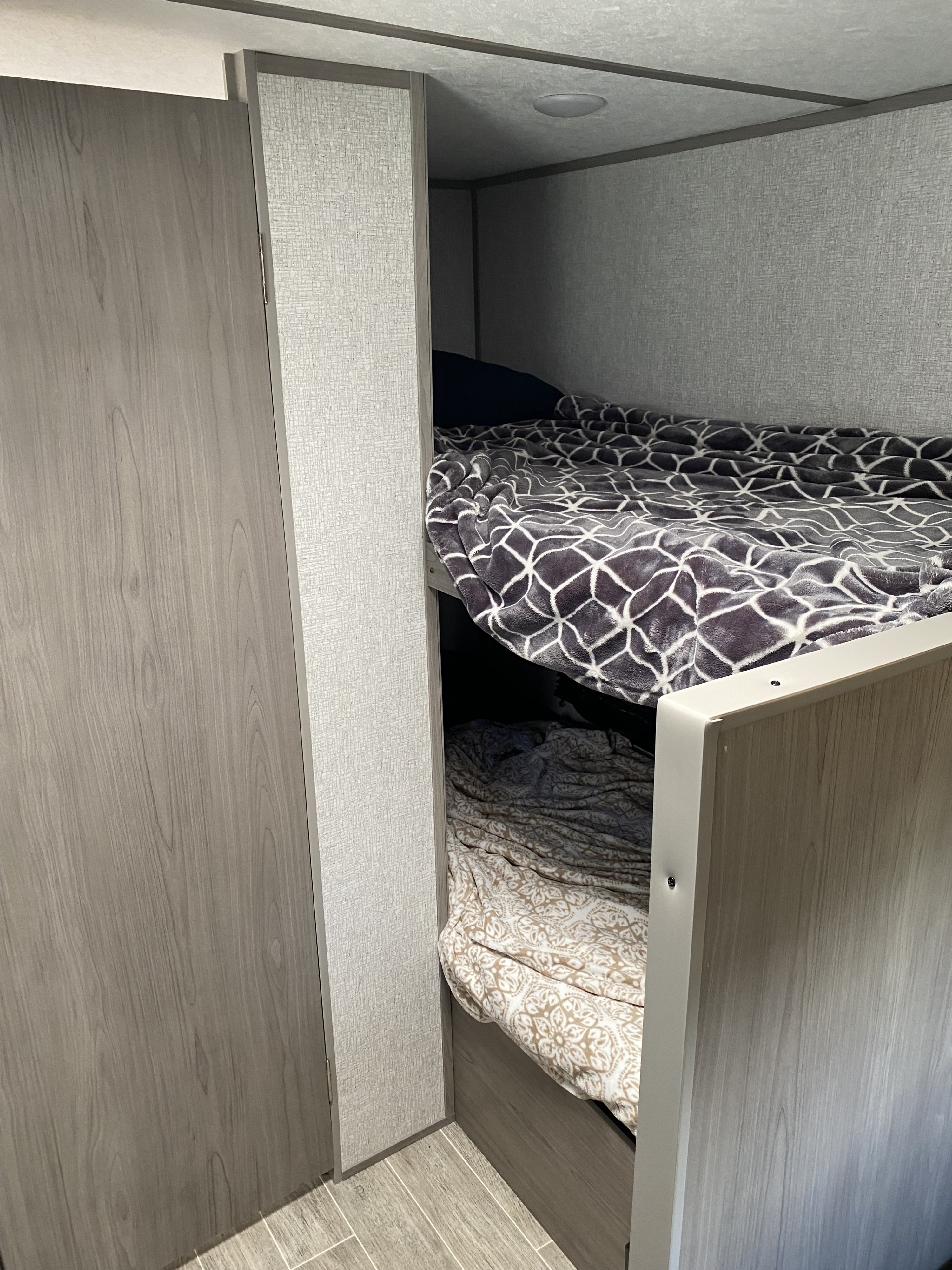 Cozy bunk beds with patterned blankets in a modern RV rental, featuring light wood finishes and textured walls.. Coleman Lantern LT 17B 2022