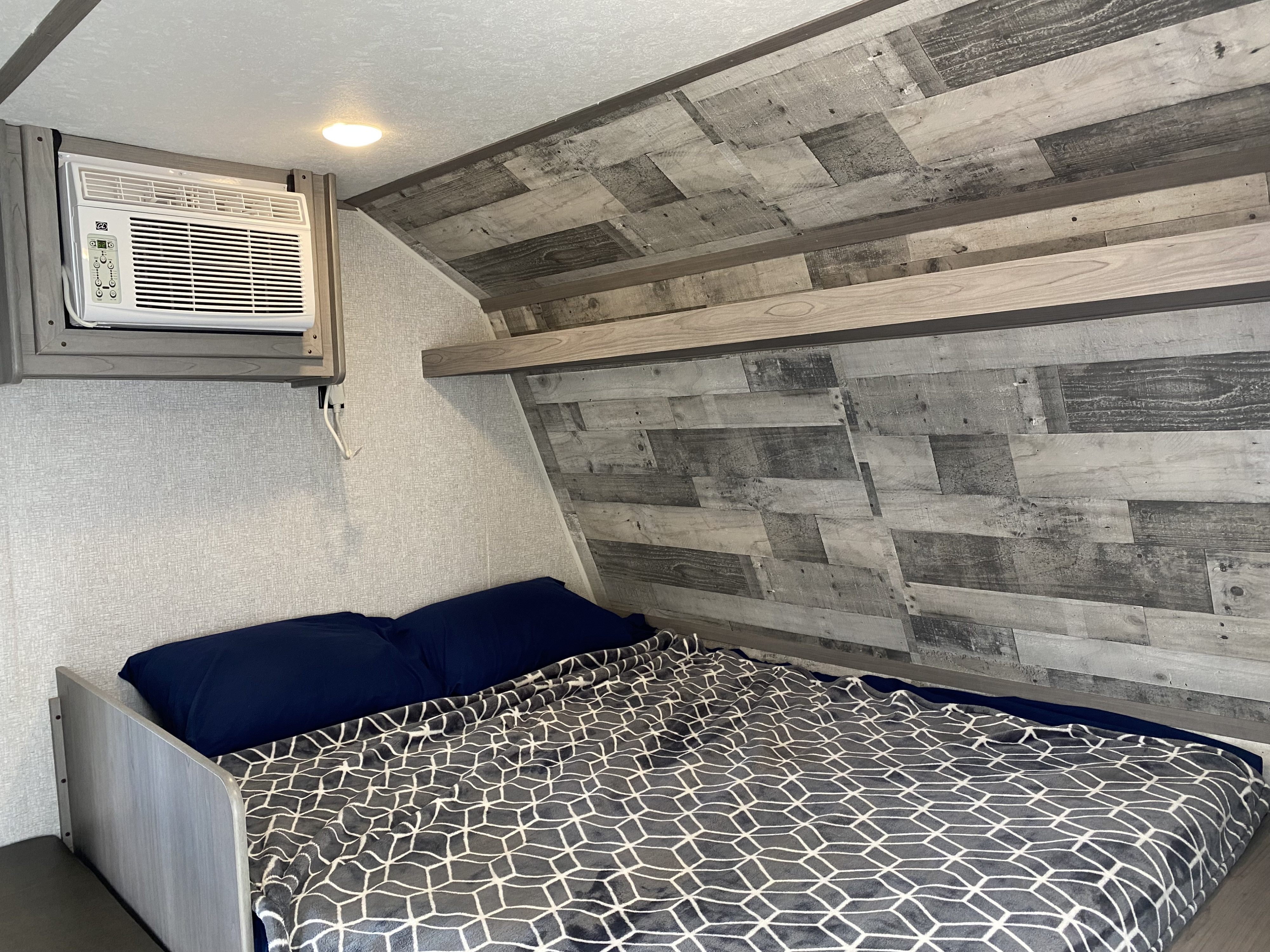Cozy RV rental bedroom with geometric blanket, AC unit, and rustic wood-paneled walls.. Coleman Lantern LT 17B 2022