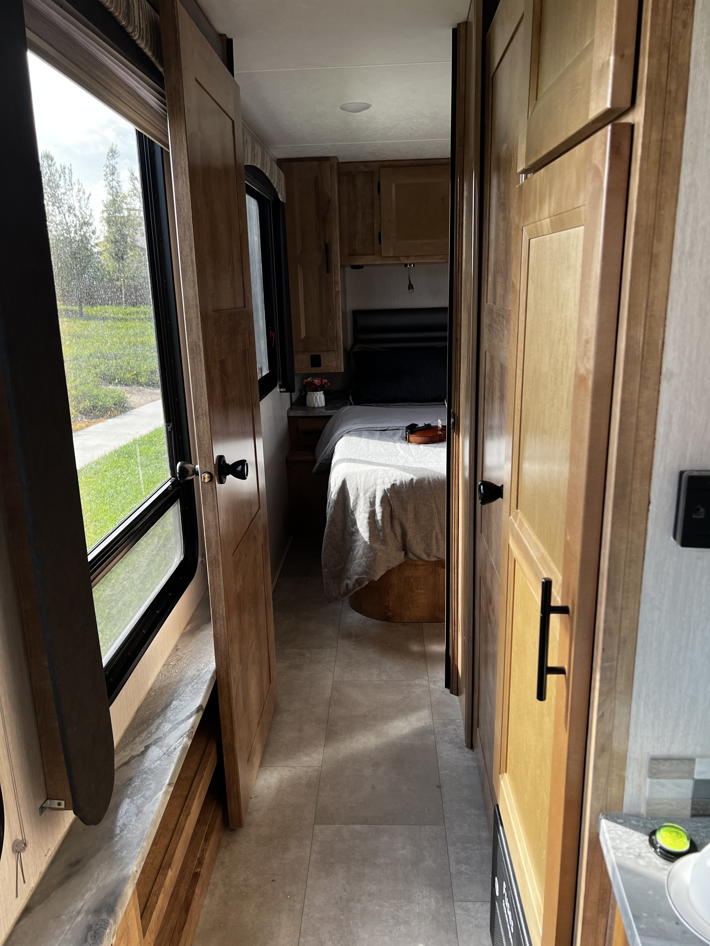 Explore this cozy RV rental interior, featuring a bright hallway leading to a compact bedroom with a bed and window view.. Coachmen Leprechaun 2021