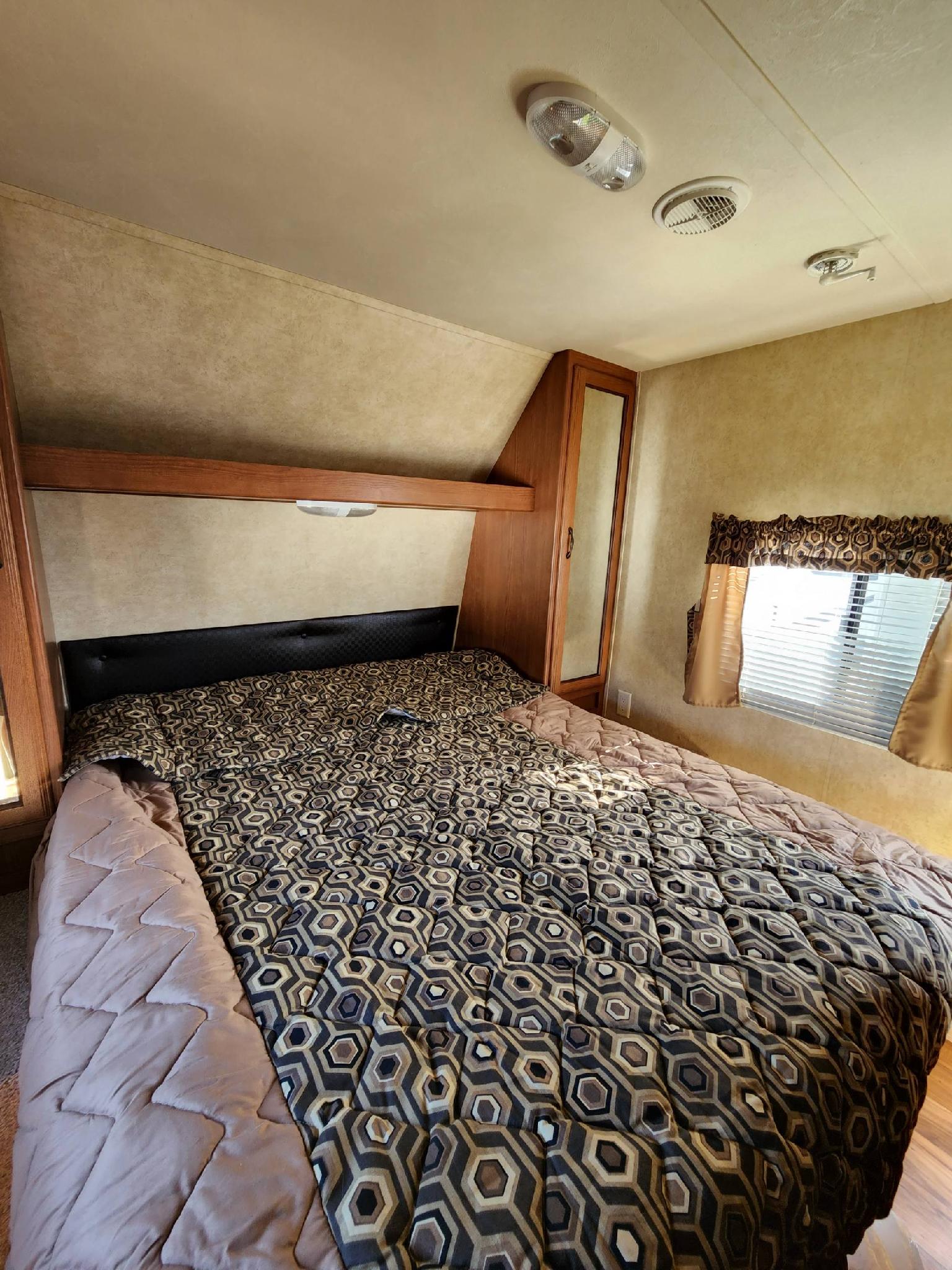 Experience comfort in this RV rental bedroom: features a full bed with a geometric comforter, overhead storage, and window.. Forest River Wildwood 2014