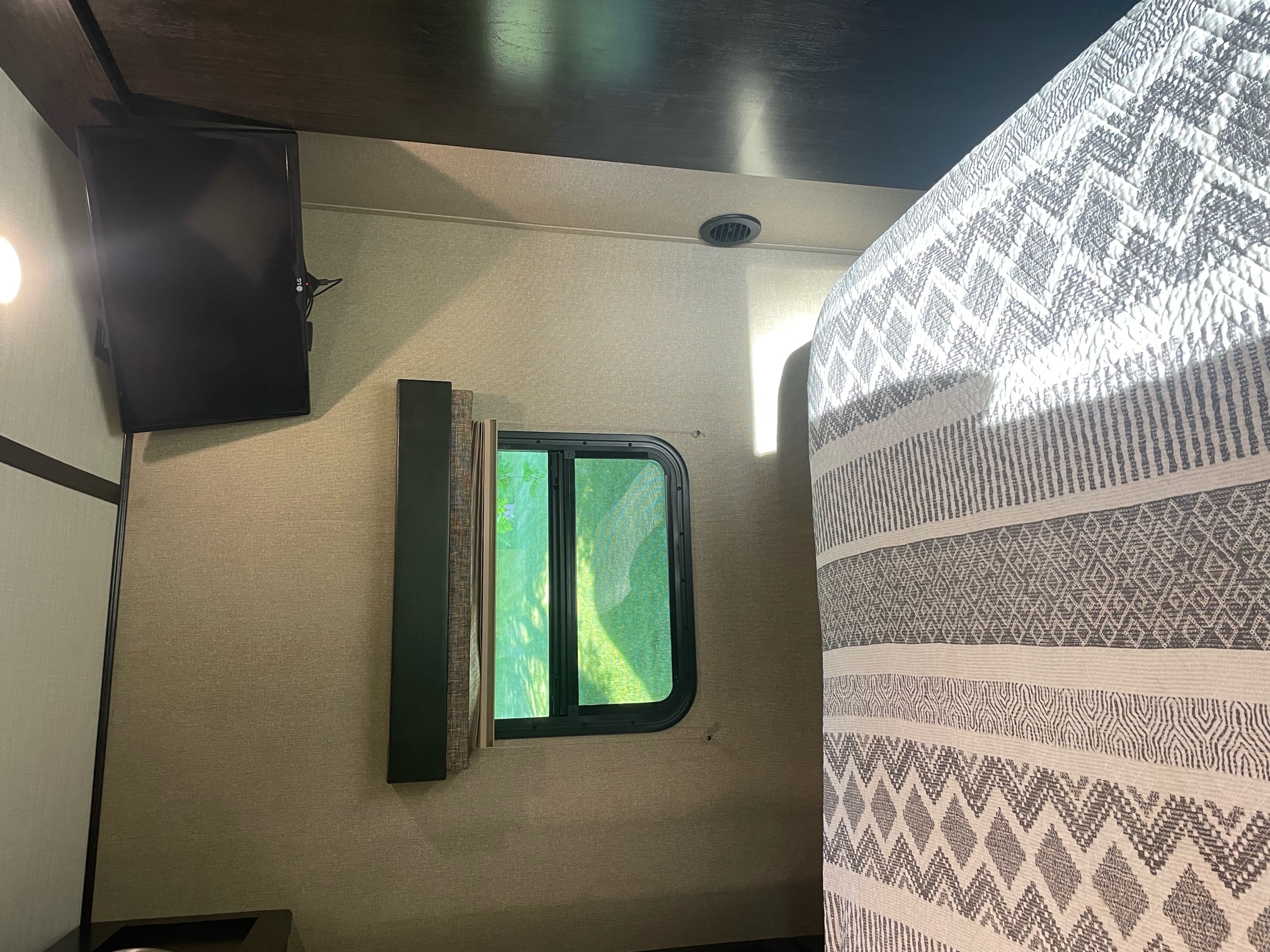 Cozy RV rental bedroom interior, featuring a wall-mounted TV, window view, and patterned quilt for comfortable travel.. Grand Design Imagine 2018