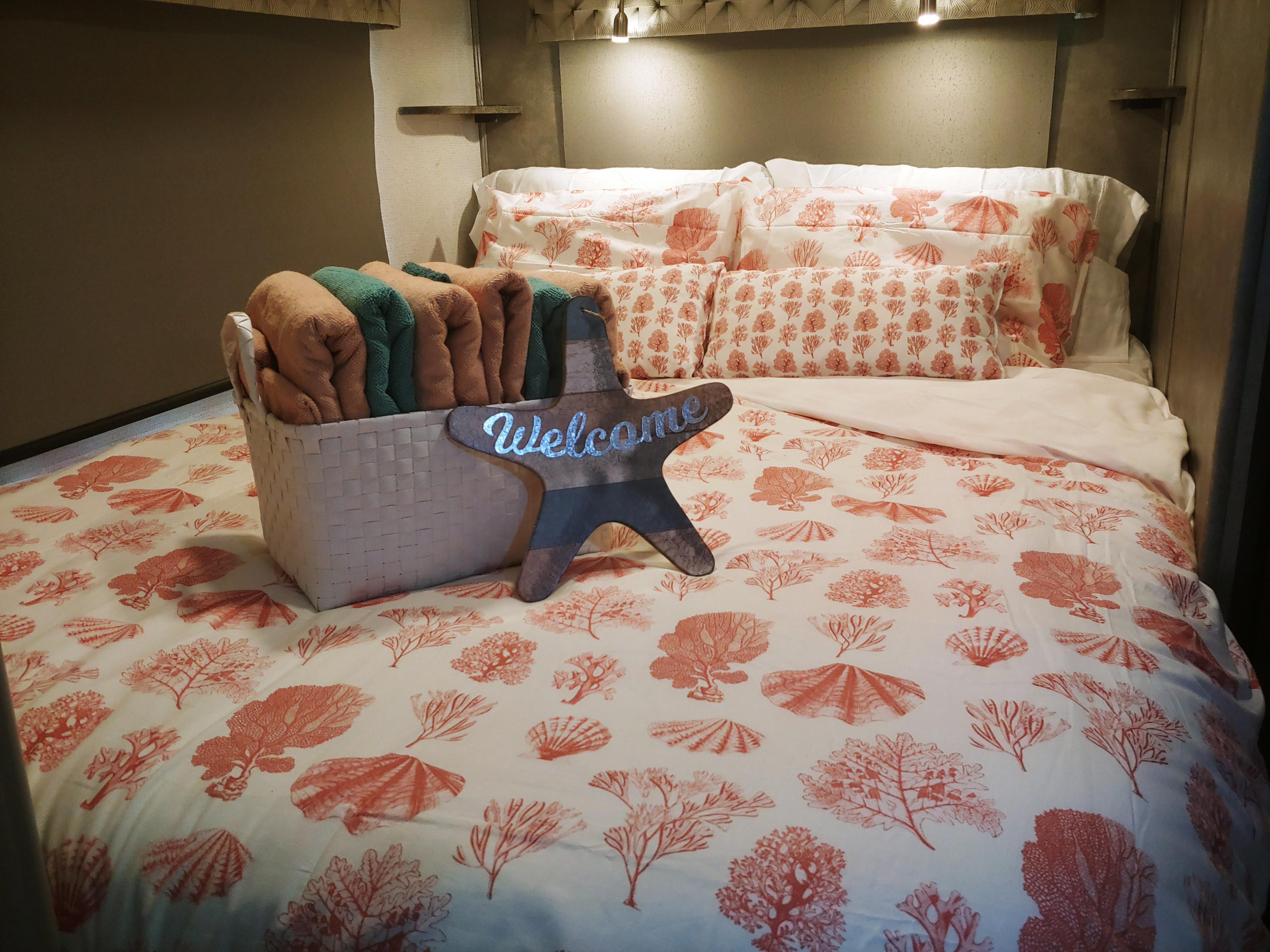 Cozy RV rental bed with coral and seashell patterned bedding, welcoming towels, and a starfish sign.. Forest River Sunseeker 2350LE 2022