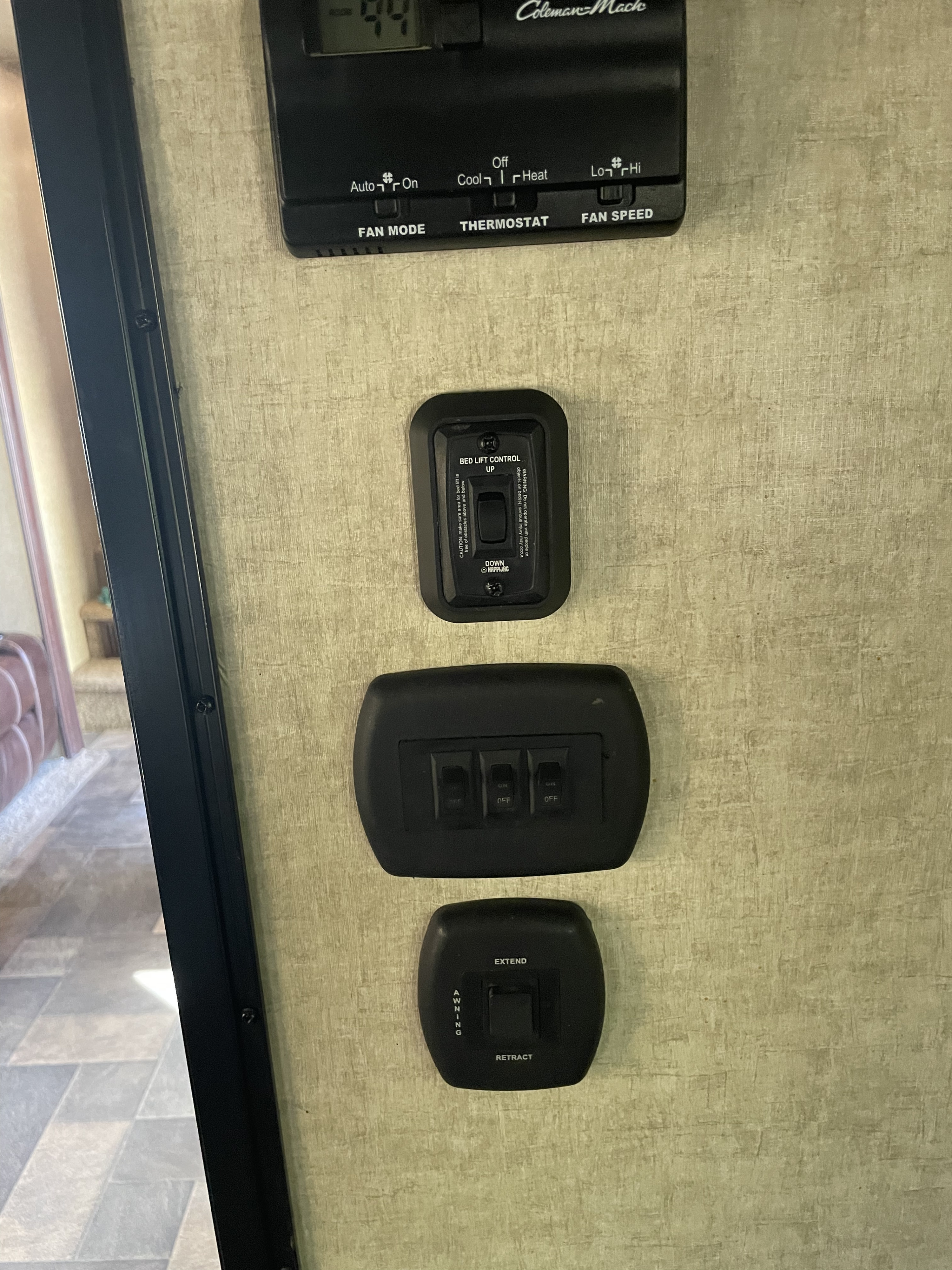 RV rental interior wall panel with a Coleman-Mach thermostat, bed lift, light, and awning controls for various functions.. Keystone Impact 2016
