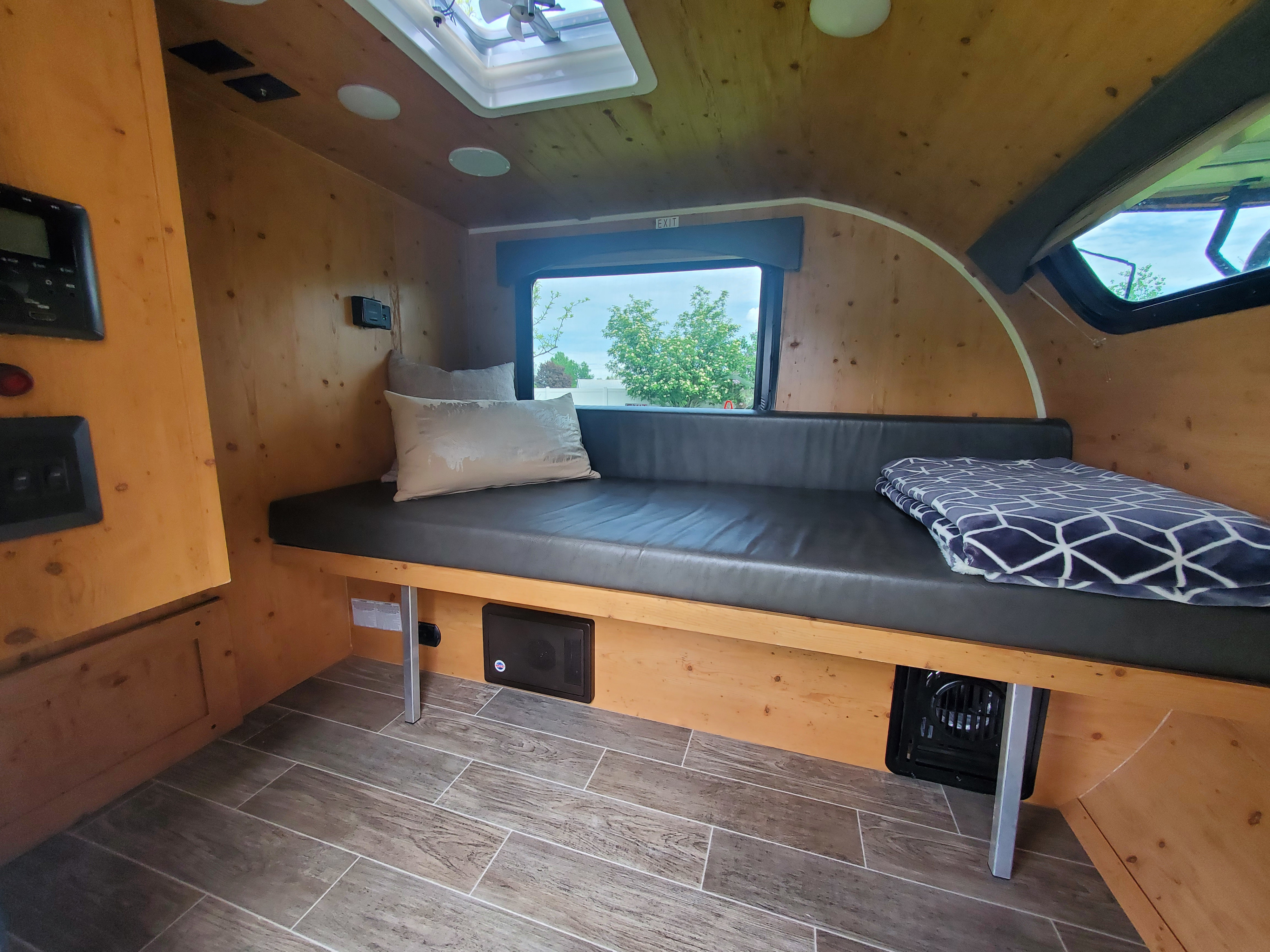 An rv rental's cozy wooden interior features a dark bench with pillows, an overhead fan, and controls for comfort.. Sunray 109 2021