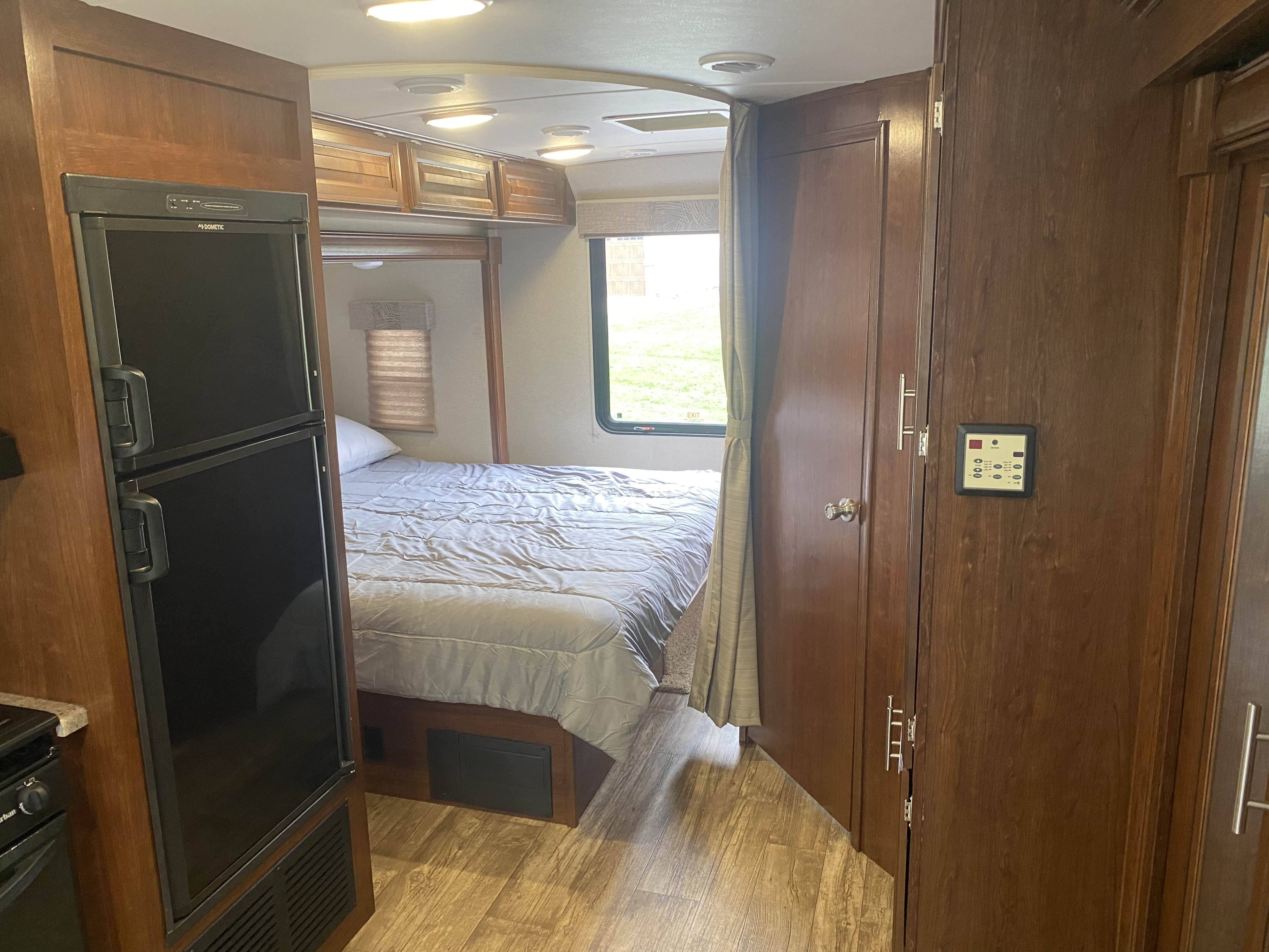 RV rental interior with a cozy bed, Dometic fridge, and wood cabinetry.. Forest River 23DS 2018