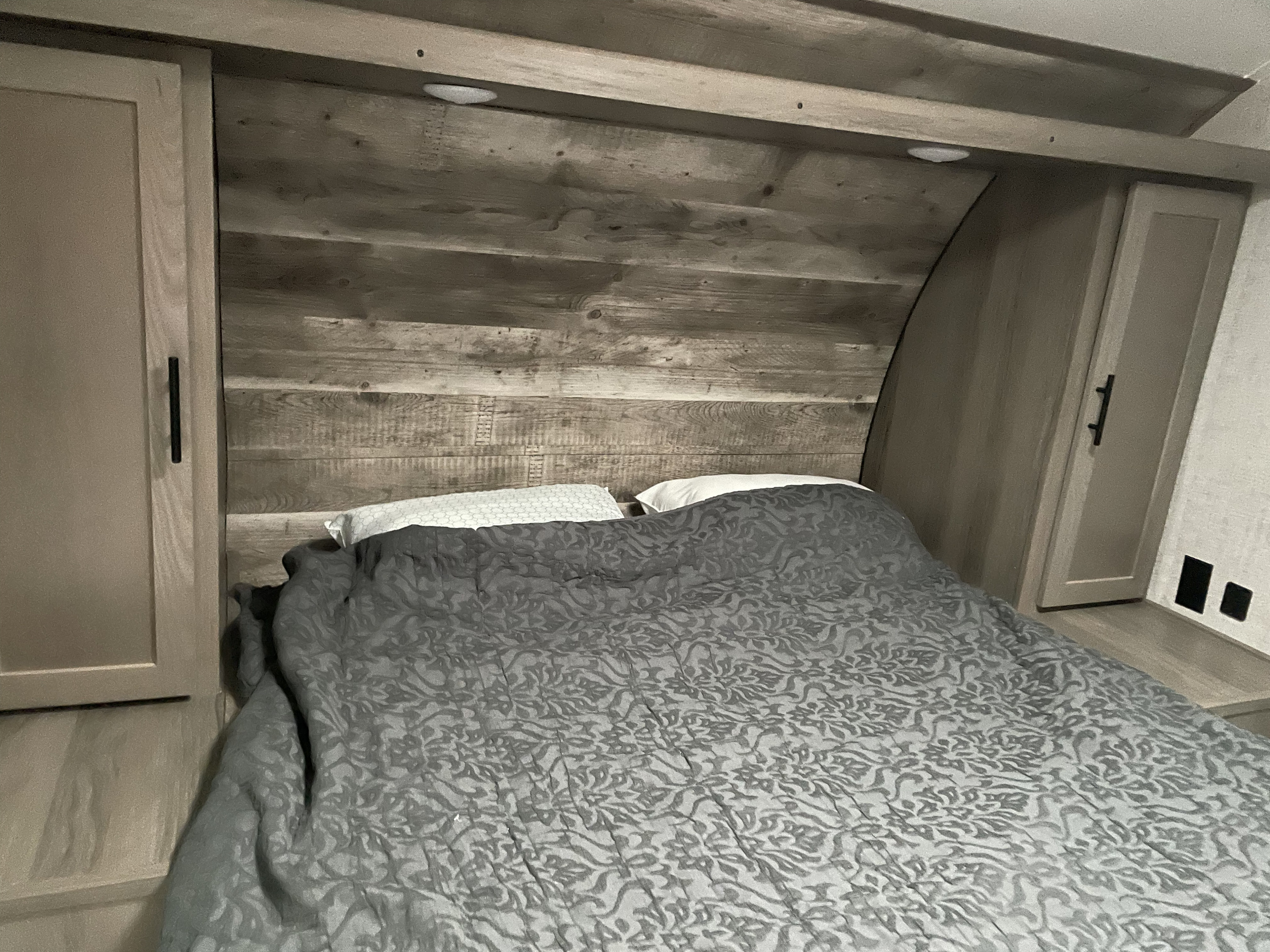Cozy RV rental bedroom featuring a rustic wood headboard, gray patterned comforter, and built-in storage on both sides.. Gulf Stream Ameri Lite 279BH 2022