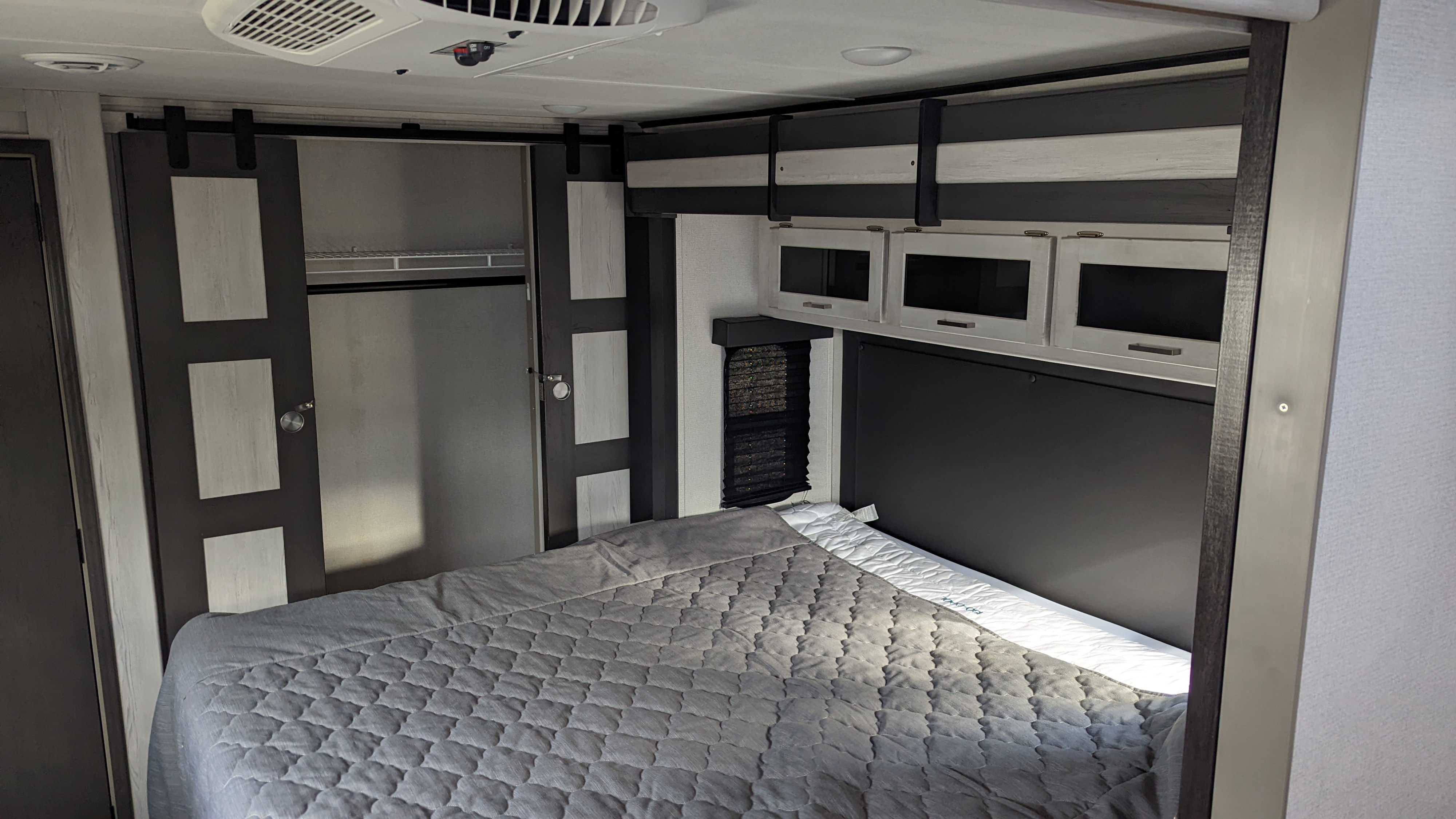 Spacious RV rental bedroom featuring a bed, overhead storage, and a barn-style closet door.. Keystone RV Sprinter Limited 2021