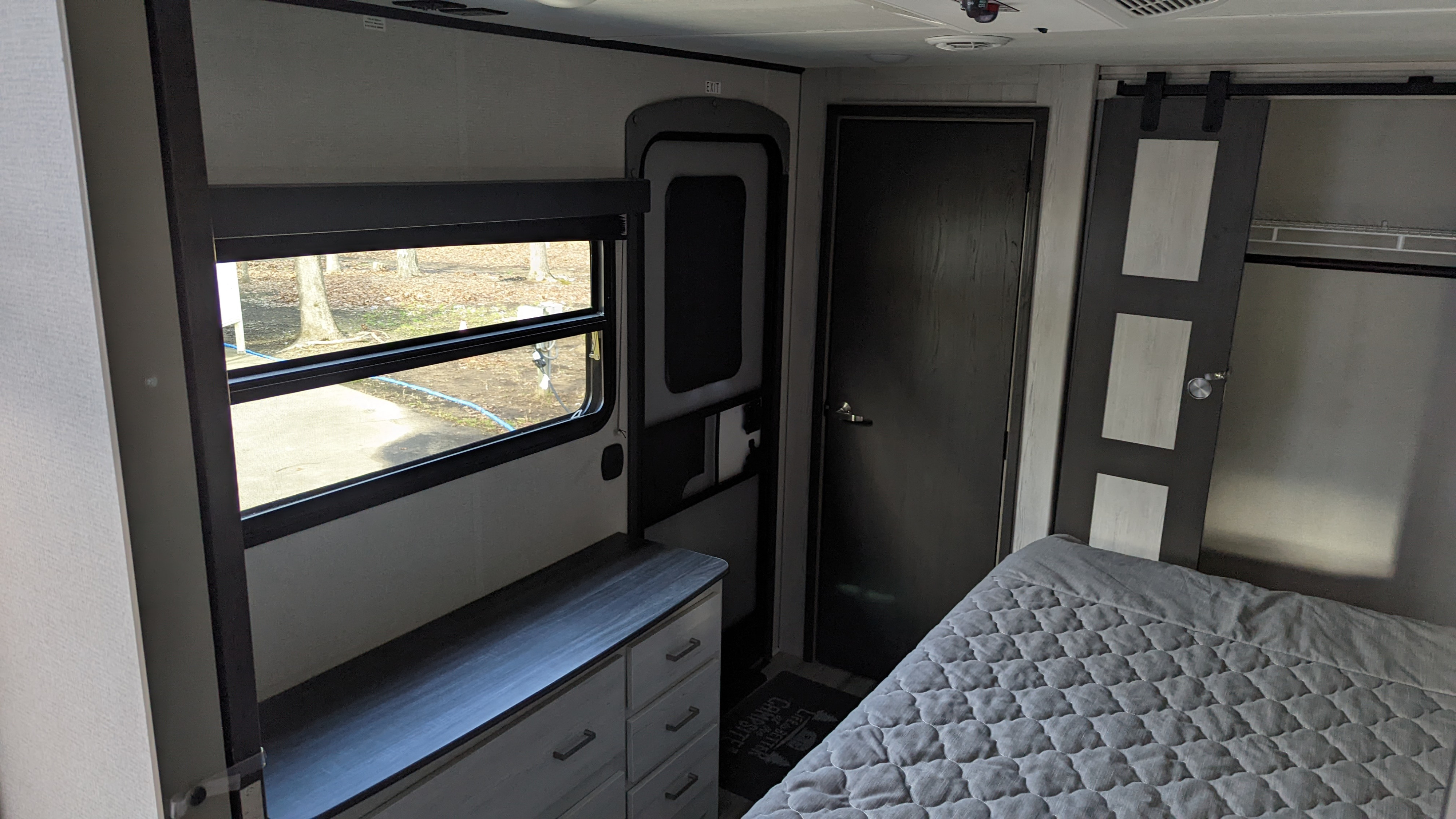Cozy RV rental interior: bedroom area with bed, dresser, window, and barn door closet. Perfect for your next adventure.. Keystone RV Sprinter Limited 2021