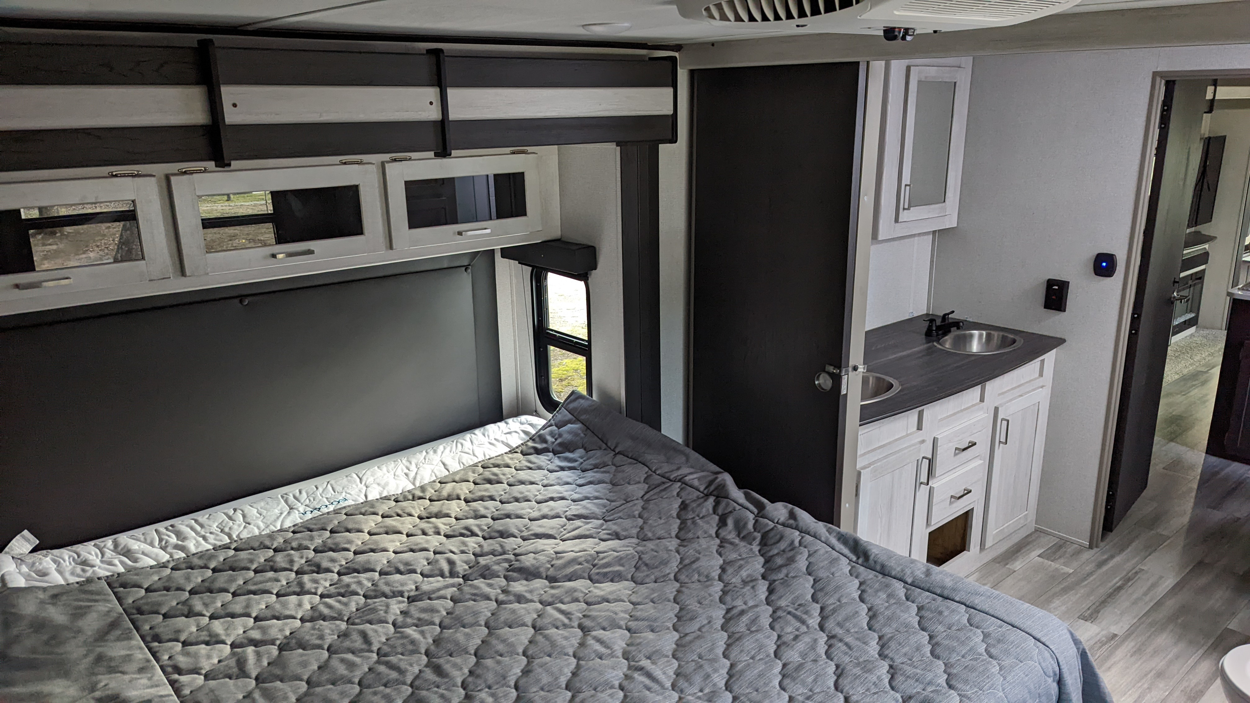 Experience comfort in this RV rental bedroom: cozy bed, overhead storage, and dual vanity sinks.. Keystone RV Sprinter Limited 2021