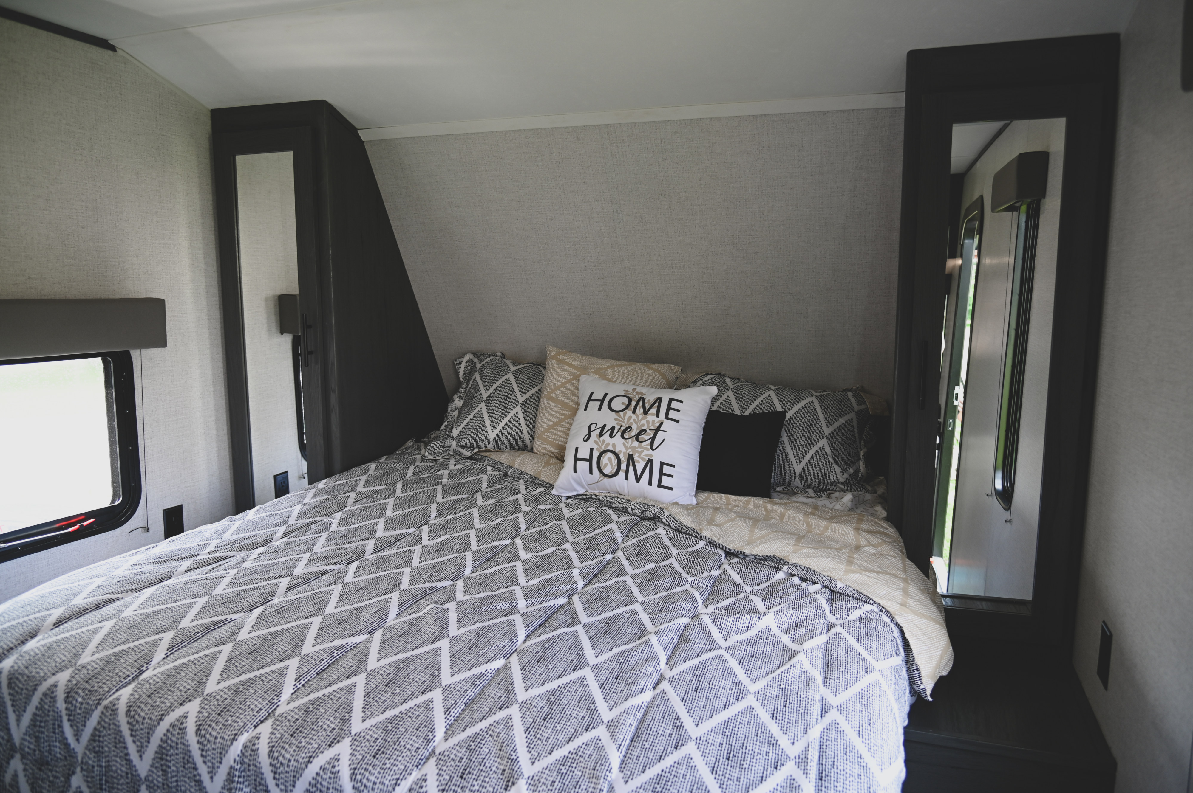 RV rental bedroom: Cozy bed with geometric bedding & a "HOME sweet HOME" pillow, featuring built-in storage and windows.. Aspen Trail LE 2021