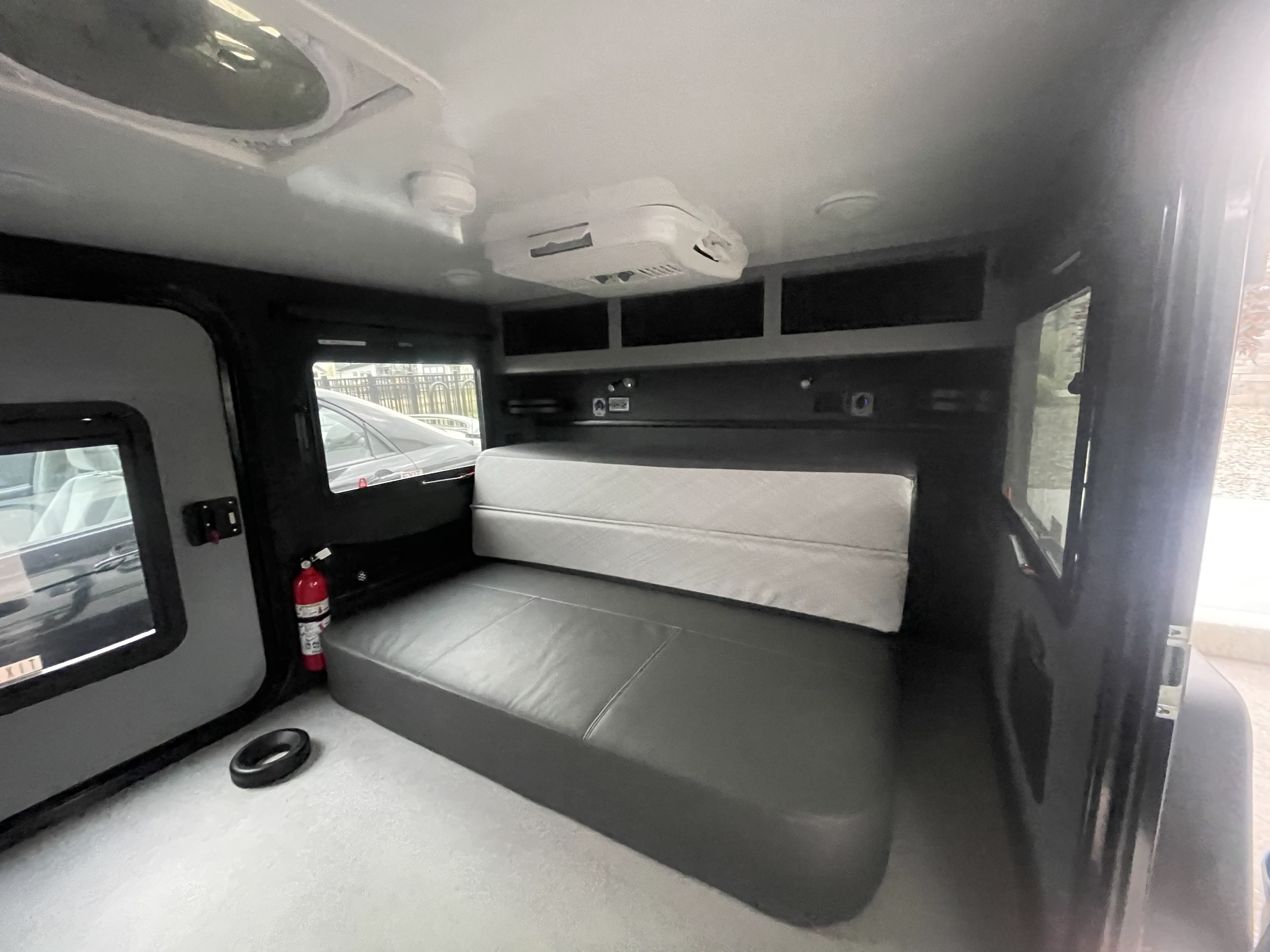 RV rental interior: compact sleeping area with gray bed, overhead storage, roof vent, & AC unit. Fire extinguisher visible.. Encore RV ROG 2022