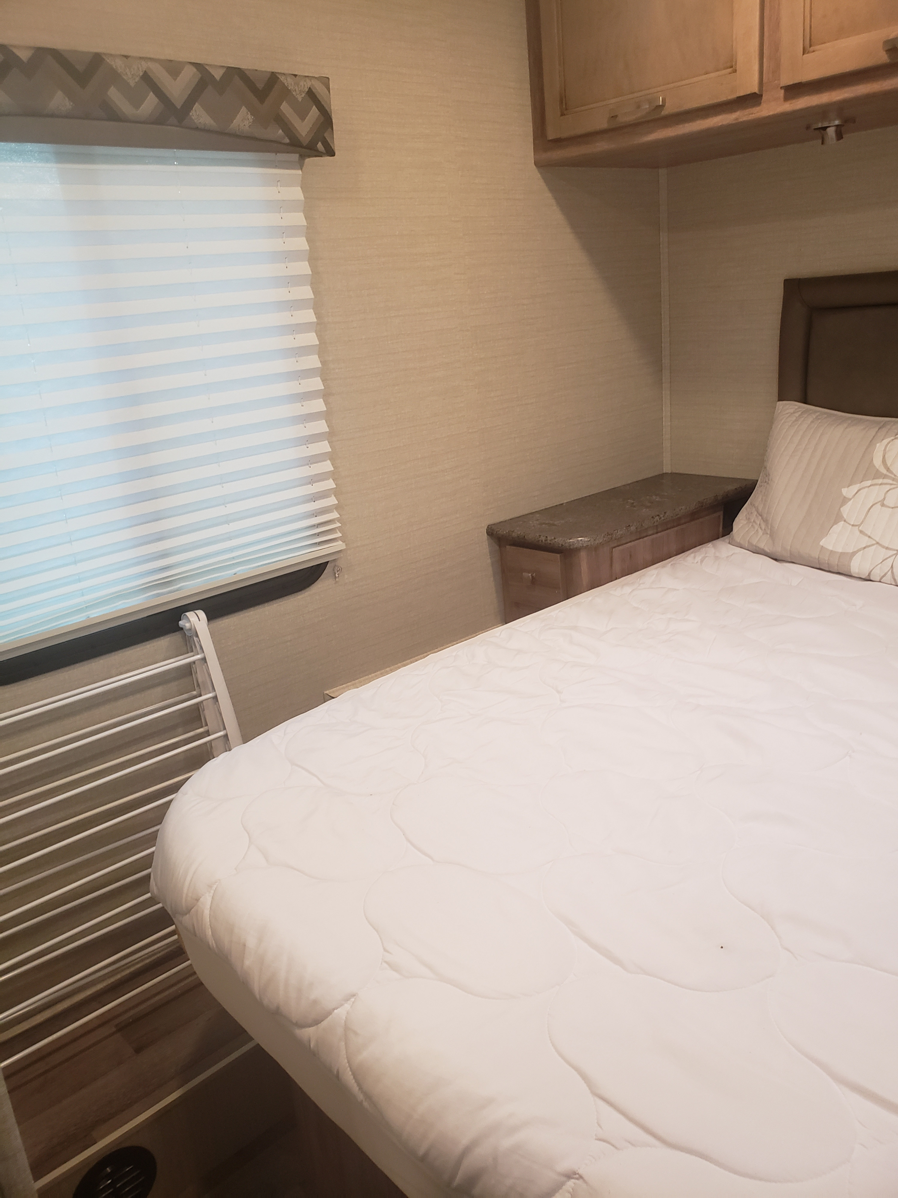 Cozy RV rental bedroom featuring a comfortable bed, overhead cabinets, and a pleated window blind for a relaxing stay.. Jayco Redhawk SE 2019