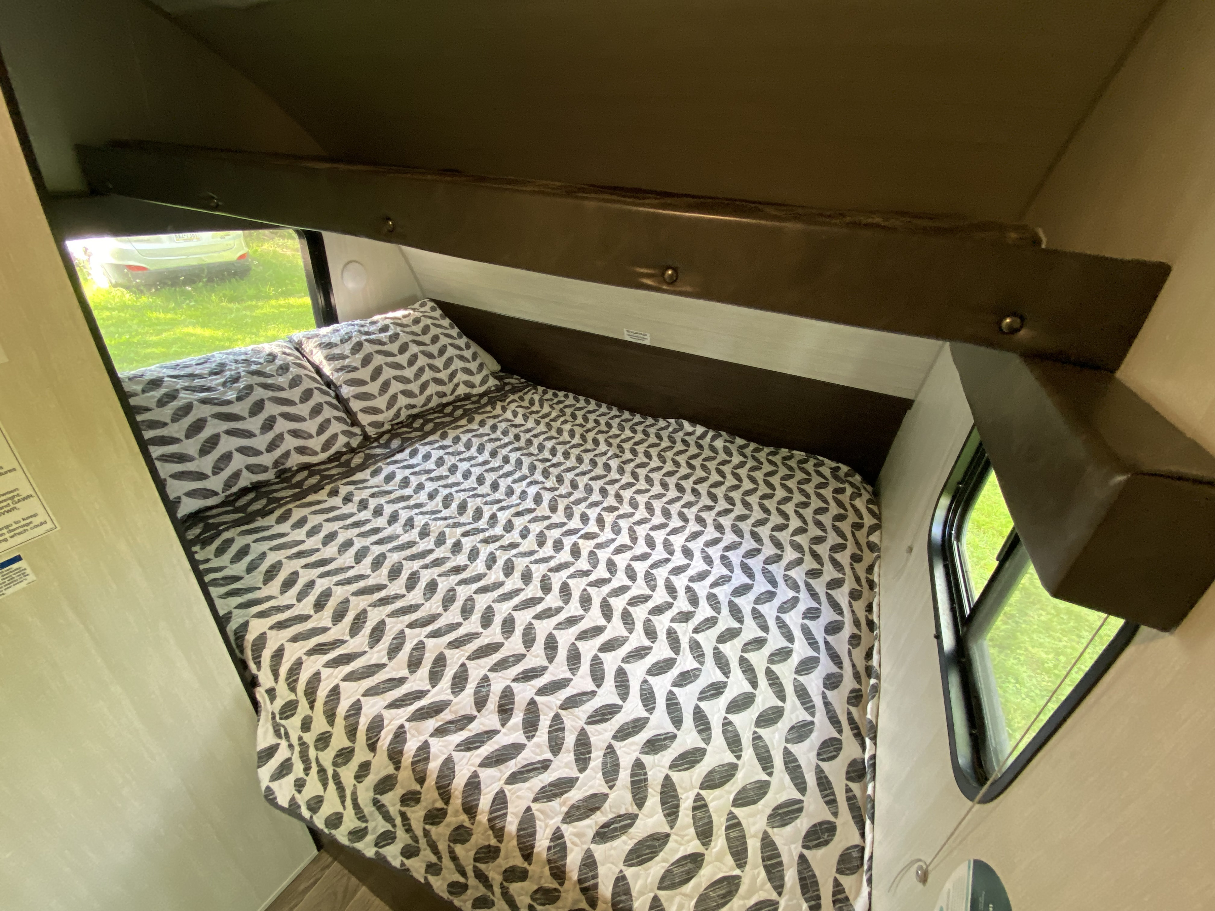 Cozy RV rental bed with modern patterned quilt and pillows. Enjoy the window view from your comfortable sleeping area.. Forest River Cherokee Wolf Pup 2019